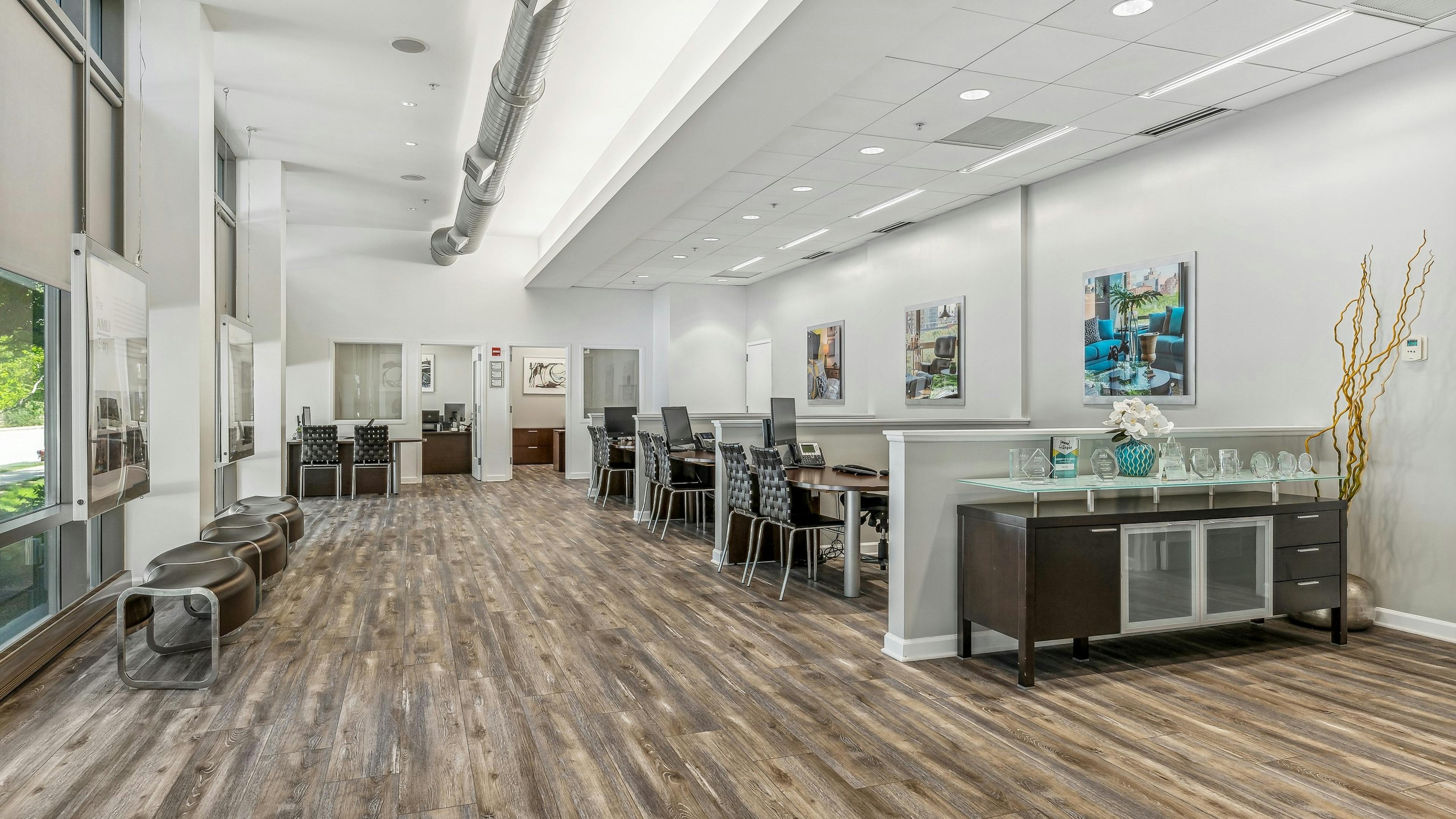 Leasing office at AMLI 900 with wood floors and desks with black chairs and a sideboard and industrial pipe along ceiling