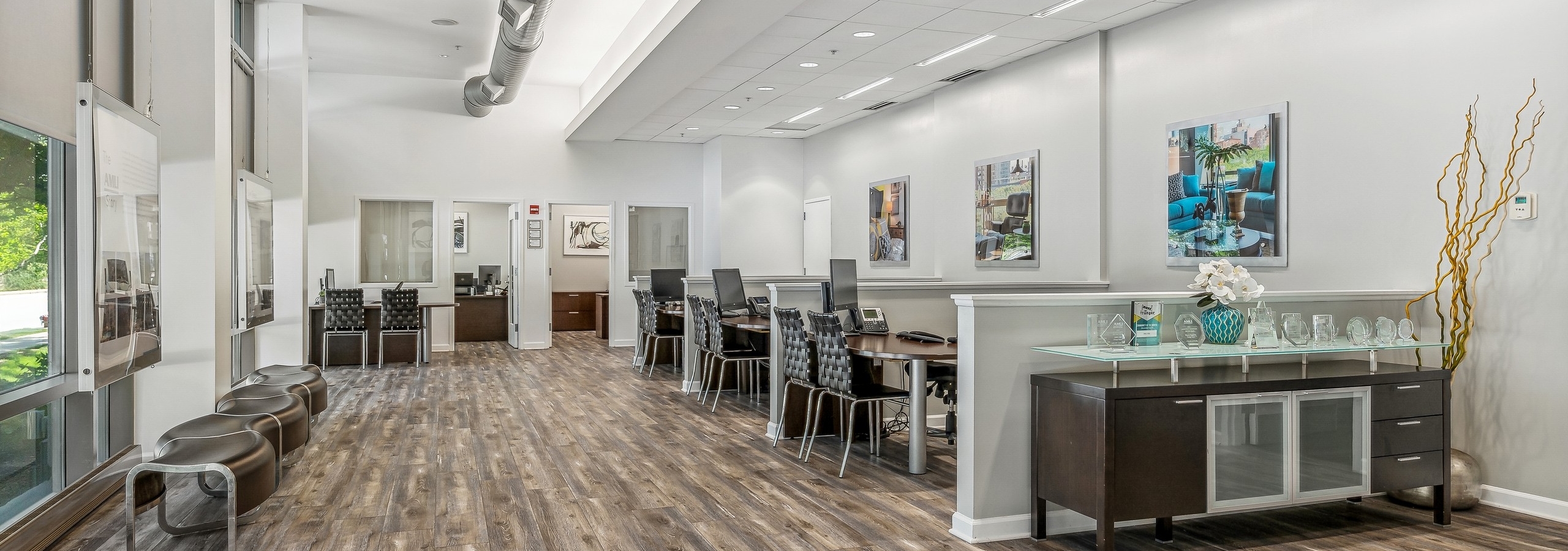 Leasing office at AMLI 900 with wood floors and desks with black chairs and a sideboard and industrial pipe along ceiling