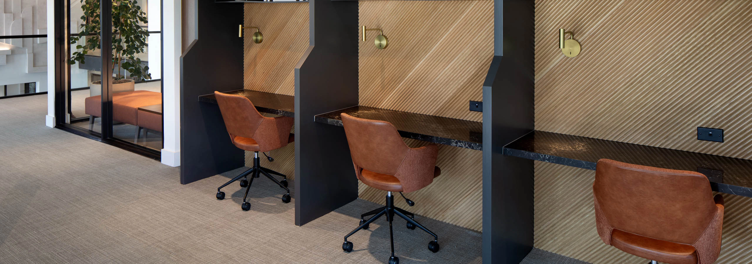 Shared workspace with private desk cubicles, rolling chairs, task lighting, wood accents, and glass-walled meeting rooms.