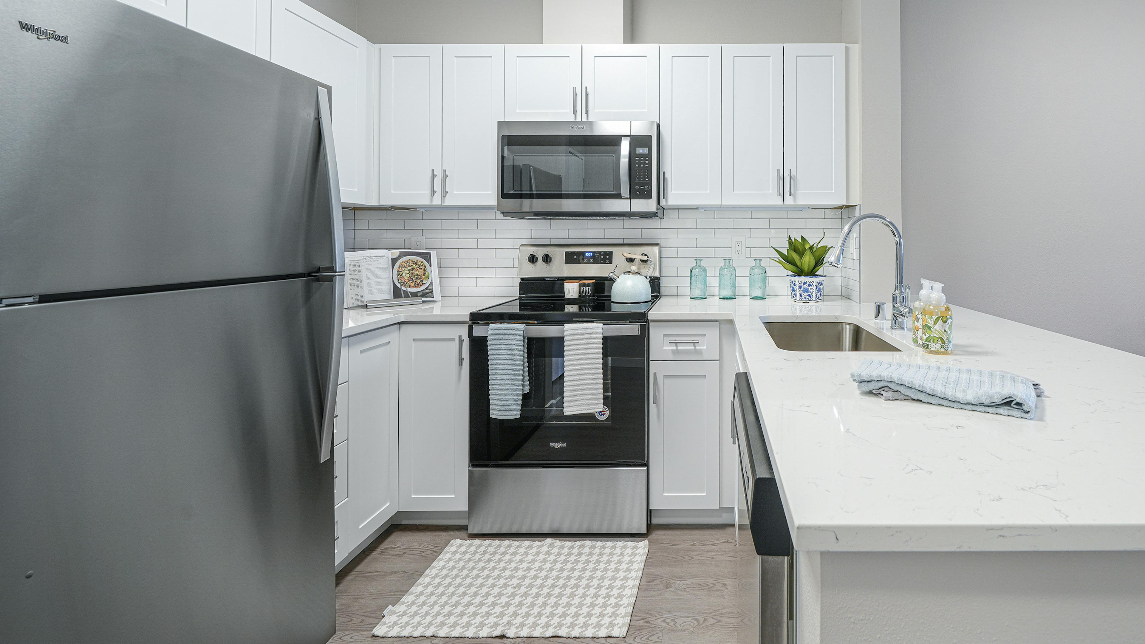 AMLI Bellevue Park apartment kitchen with stainless steel appliances and white cabinets and countertop and tiled backsplash