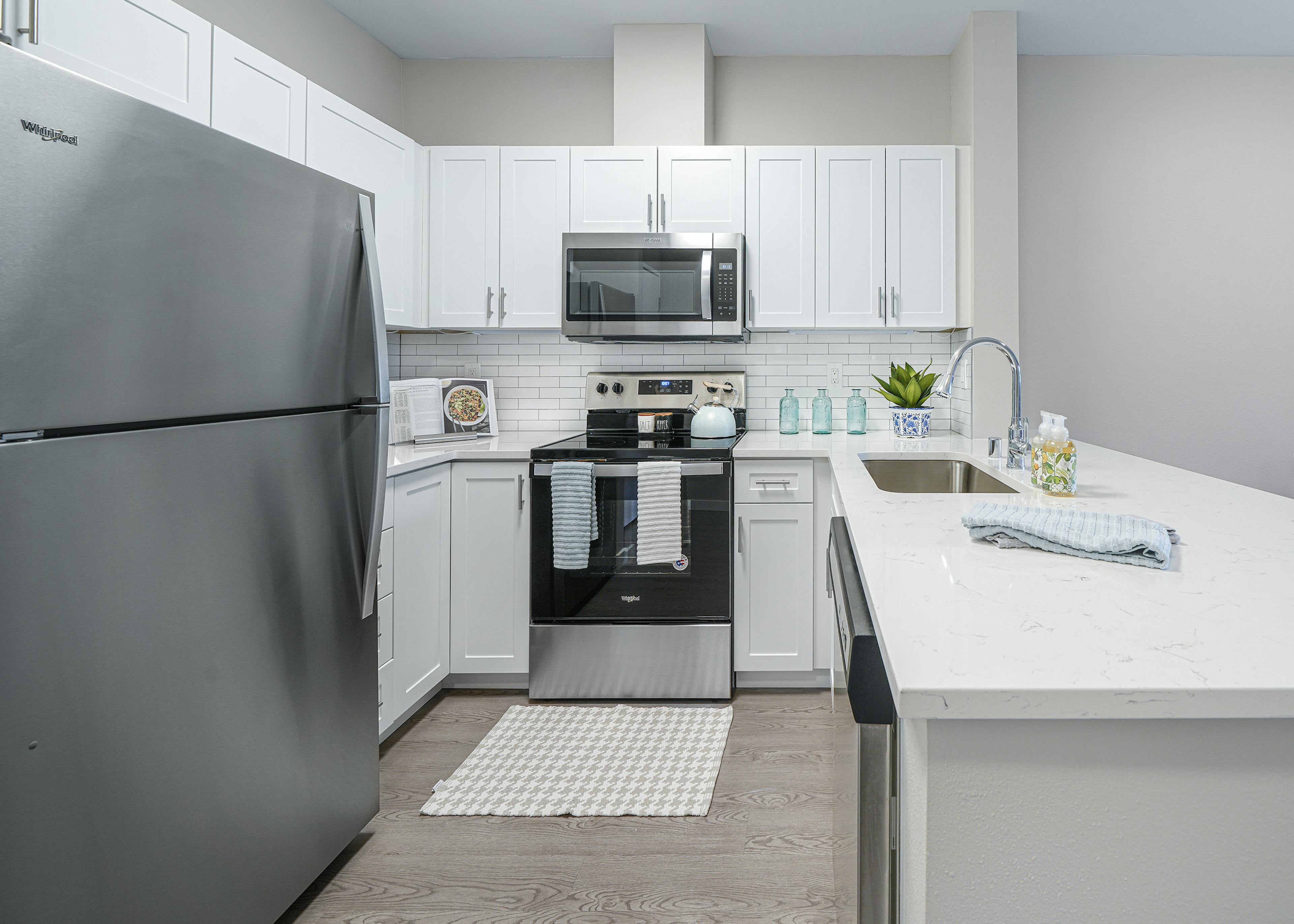 AMLI Bellevue Park apartment kitchen with stainless steel appliances and white cabinets and countertop and tiled backsplash