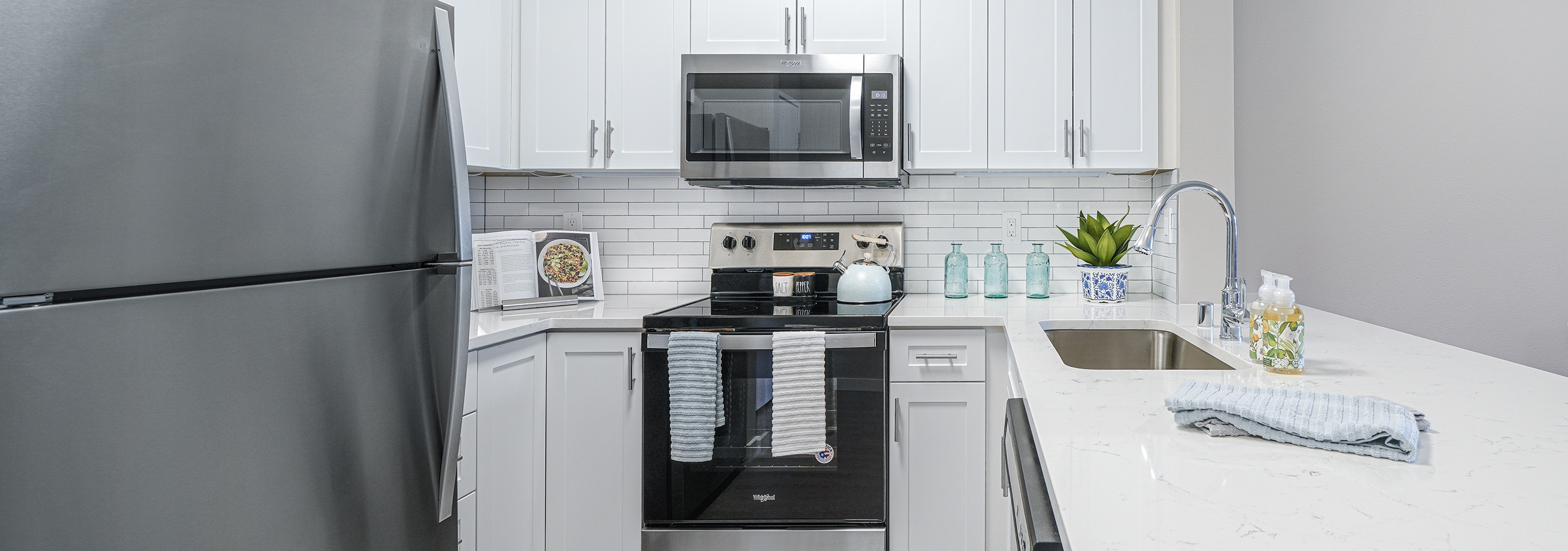 AMLI Bellevue Park apartment kitchen with stainless steel appliances and white cabinets and countertop and tiled backsplash
