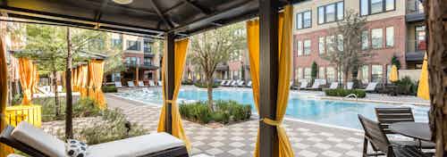 Cabana at the AMLI West Plano pool amenity with orange curtains and lounge chairs with creme cushions overlooking the water