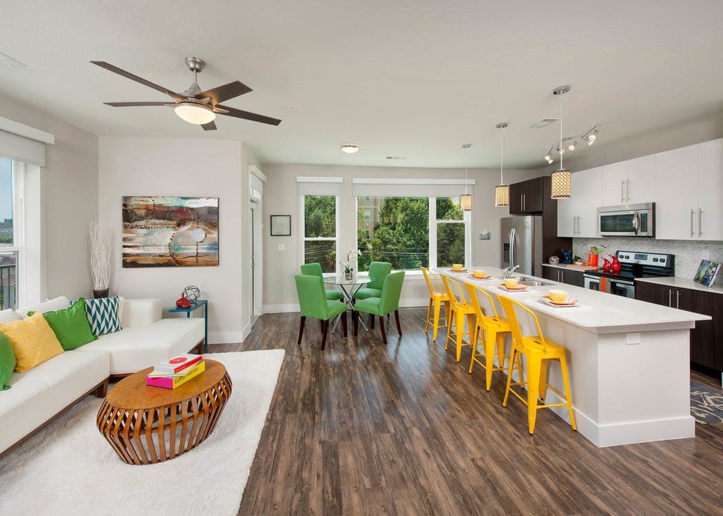 AMLI Piedmont Heights kitchen and living room with medium wood floors and long quartz countertop island with yellow barstools