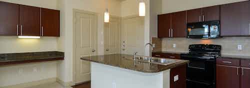 Kitchen at AMLI Inverness apartments with hardwood floor a view of an island and fridge and microwave and view of front door