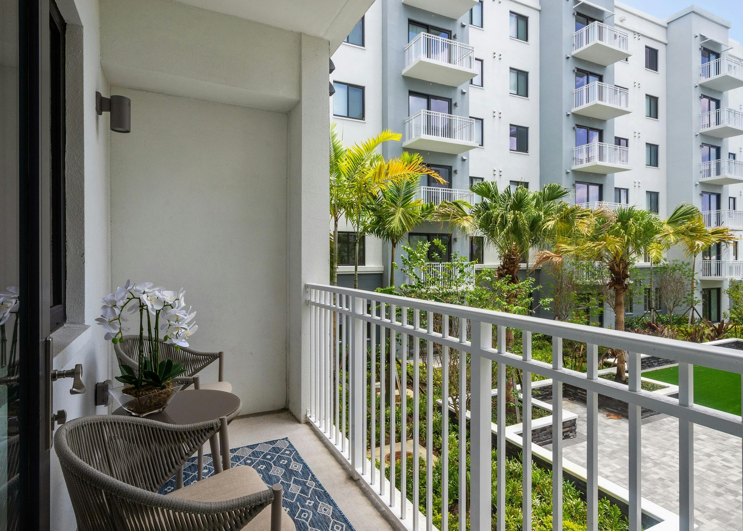 Exterior view of AMLI Park West apartment balcony with white metal bars and gray table and 2 chairs and a view of courtyard