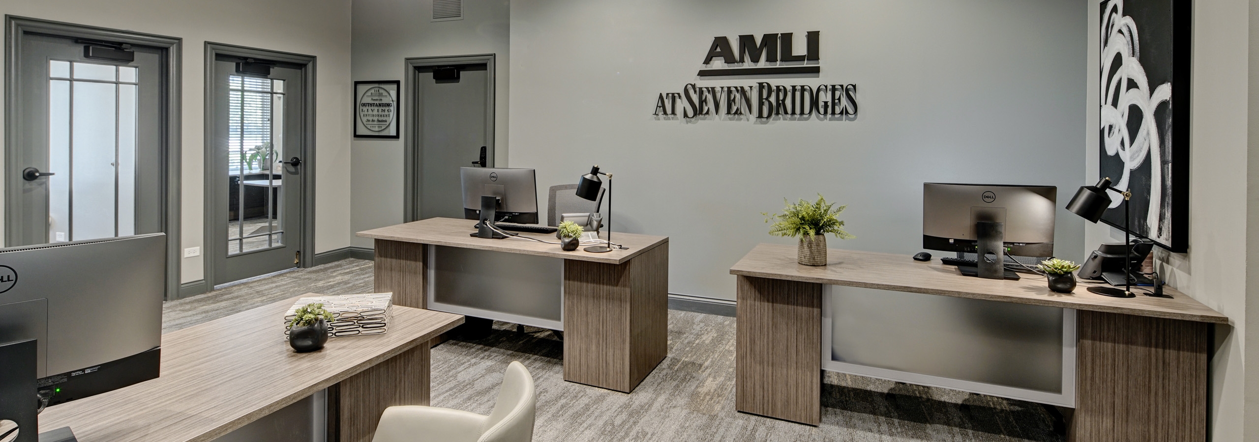 Leasing office of AMLI at Seven Bridges with 3 desks with computers and community logo on gray wall and doors to private offices