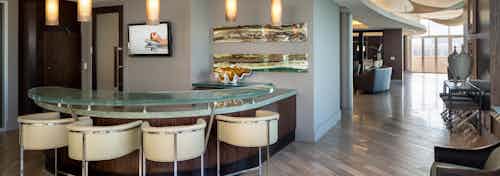 AMLI Design District sky lounge entry with glass bar counter with four white tools and TV and 5 pendant lights hanging above
