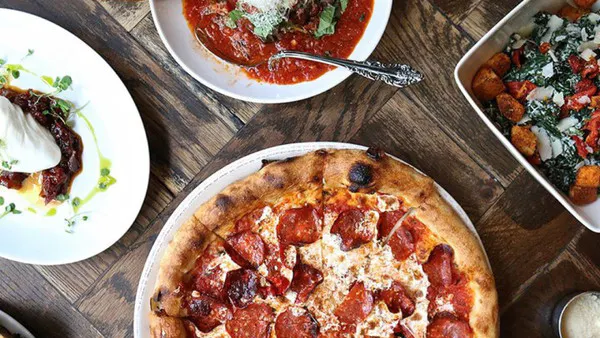 Overhead view of an Italian food spread on a wooden table featuring pepperoni pizza, pasta with red sauce, and a fresh salad