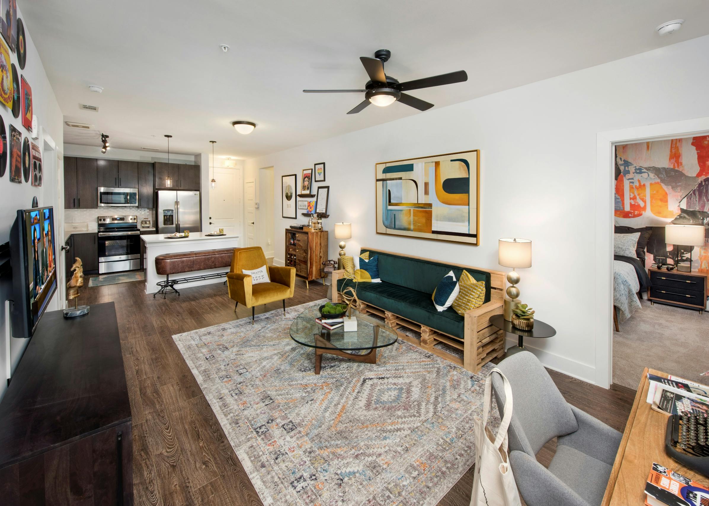 Interior view of AMLI Dectaur apartment kitchen, living room with ceiling fan and peek inside bedroom through open door.