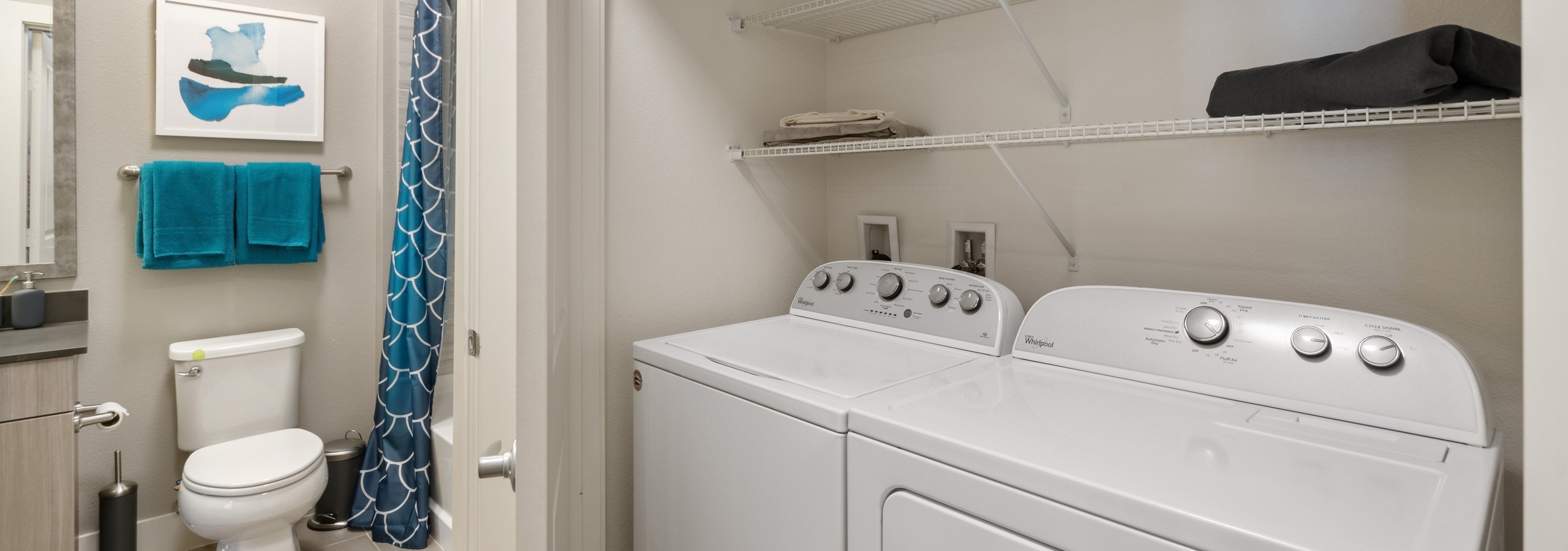 AMLI Dry Creek side by side white washer and dyer with 2 shelves inside closet with view into adjacent bathroom