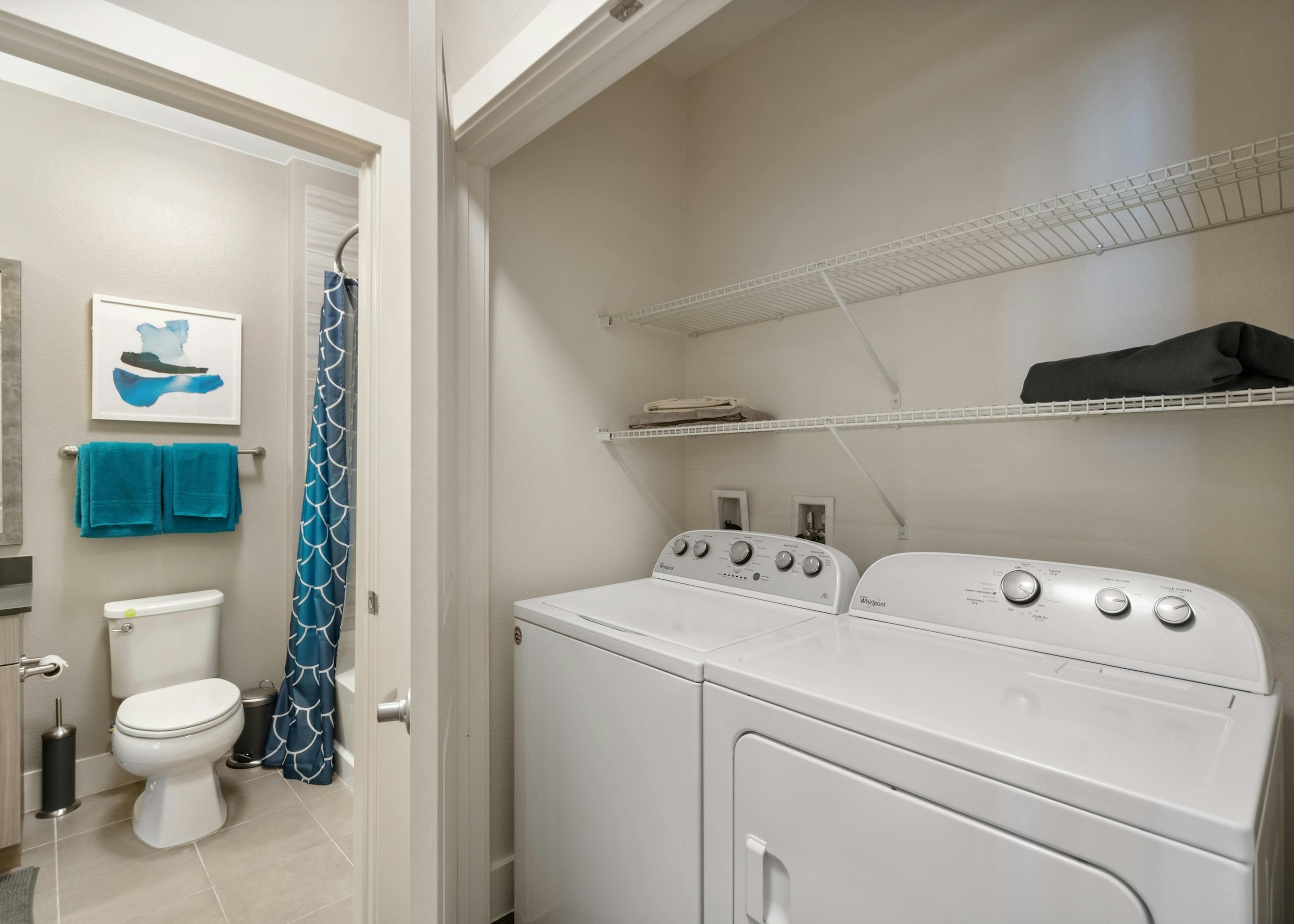 AMLI Dry Creek side by side white washer and dyer with 2 shelves inside closet with view into adjacent bathroom 