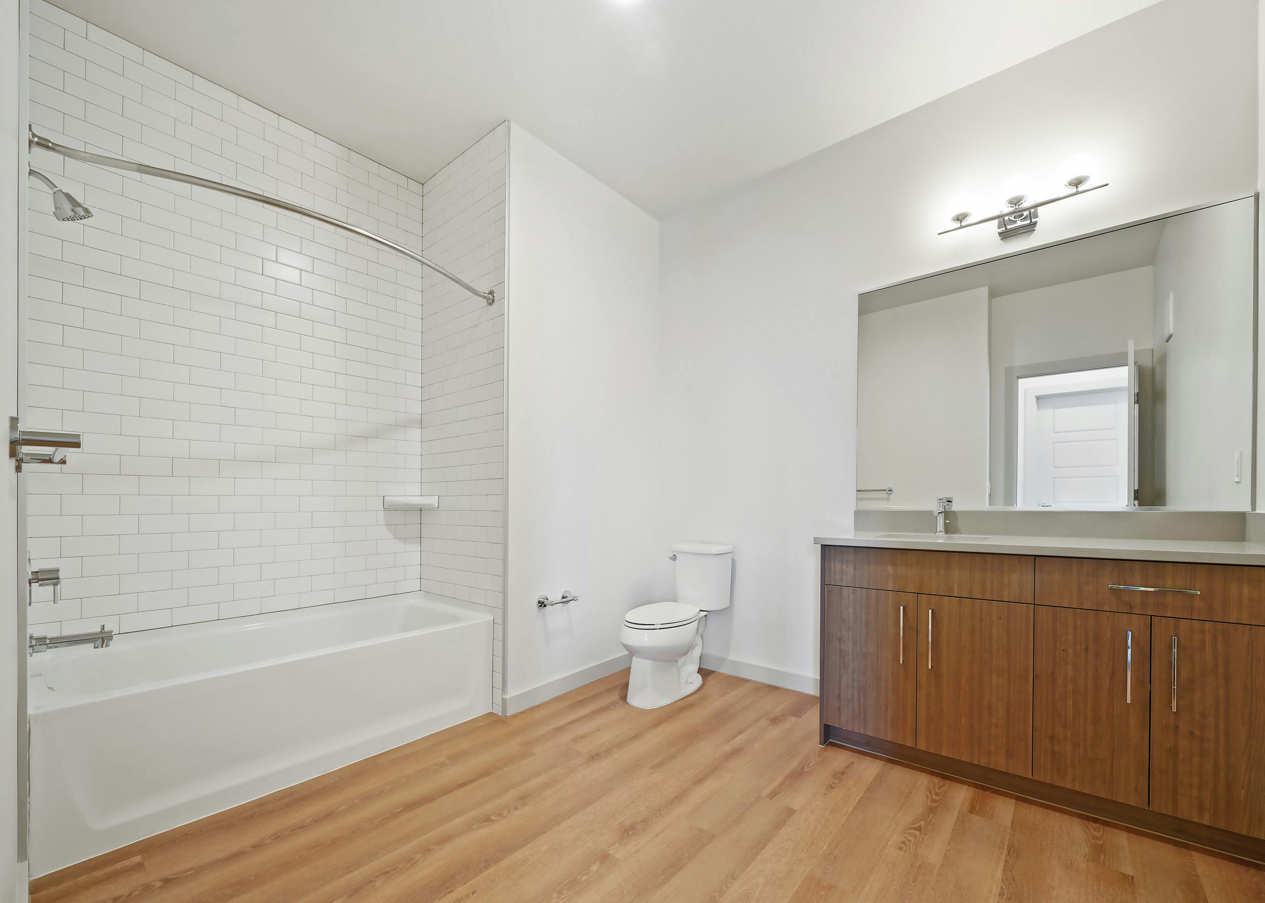 AMLI Spring District apartment bathroom with white shower and tub combination with white tile walls and toilet and vanity