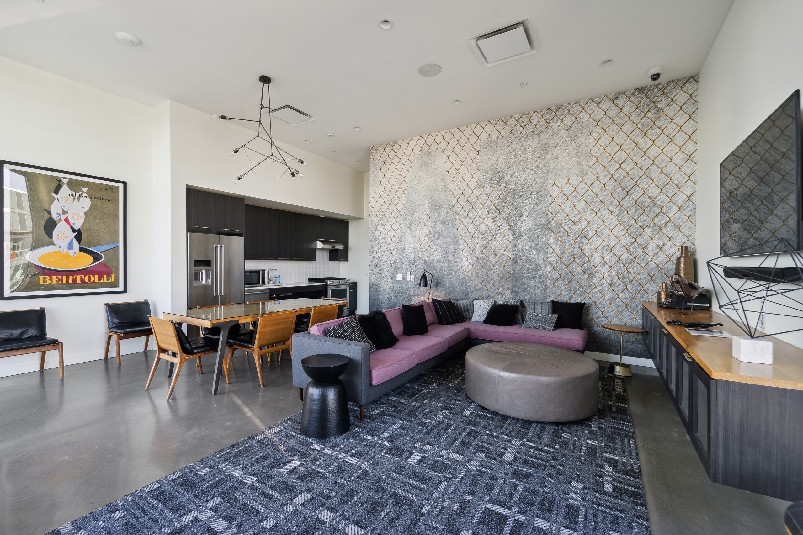 Resident lounge at AMLI Arc with purple couch on a gray pattern area rug and a kitchen with dining table and chairs