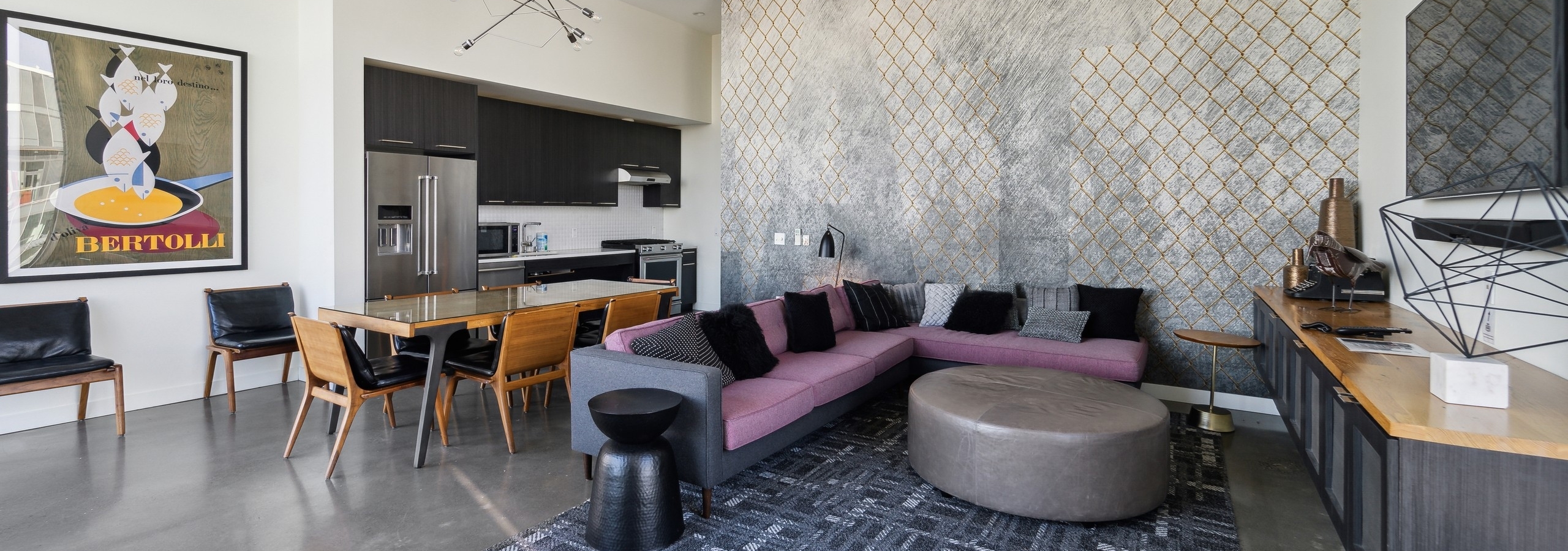 Resident lounge at AMLI Arc with purple couch on a gray pattern area rug and a kitchen with dining table and chairs
