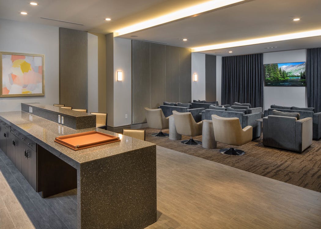 Interior of theatre at AMLI 3464 with grey seating facing large TV on the wall with a curtain and a kitchen area in the back