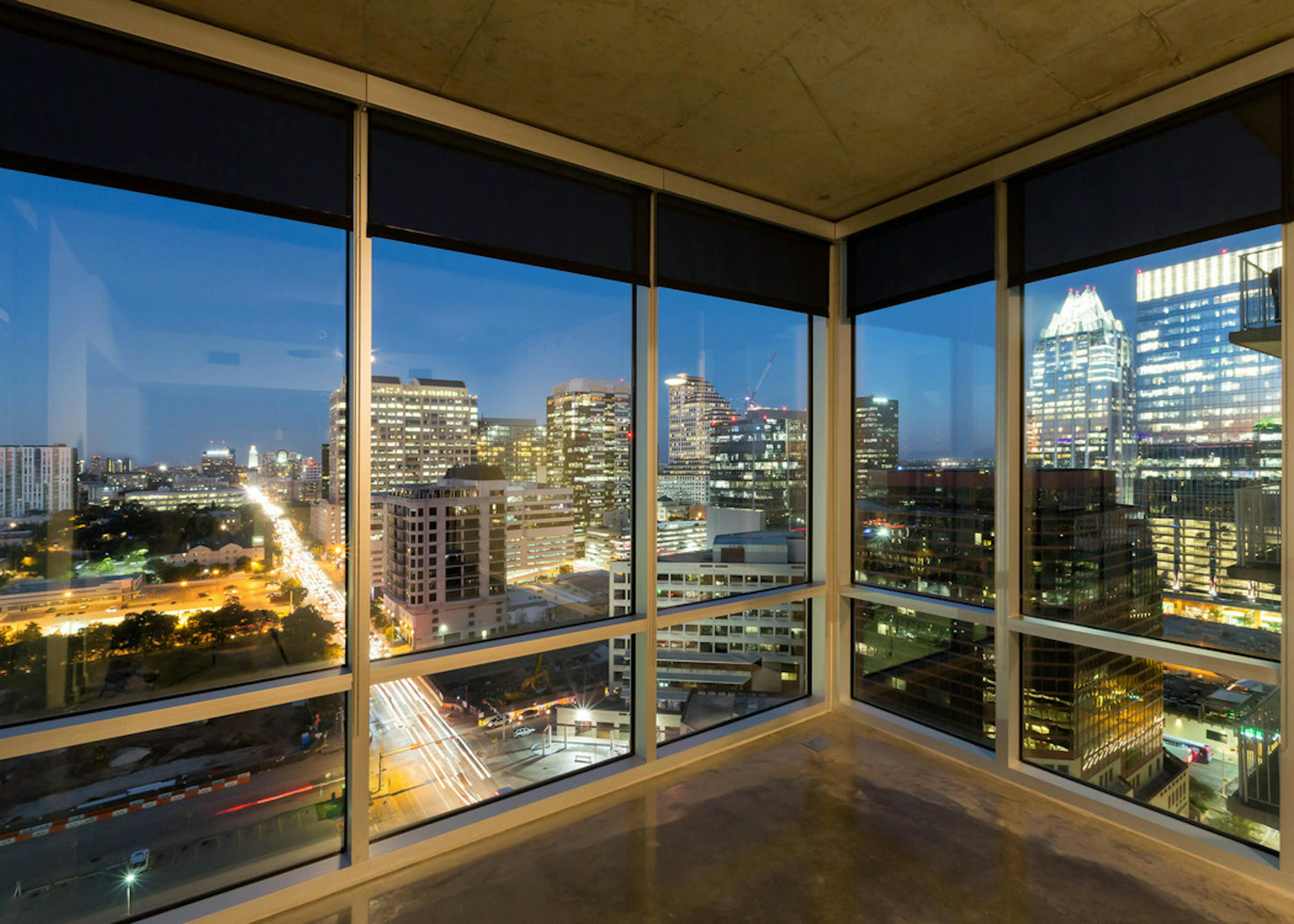 Floor to ceiling window view at AMLI on 2nd apartment community of lit up city buildings and landscaping and busy roads at nighttime