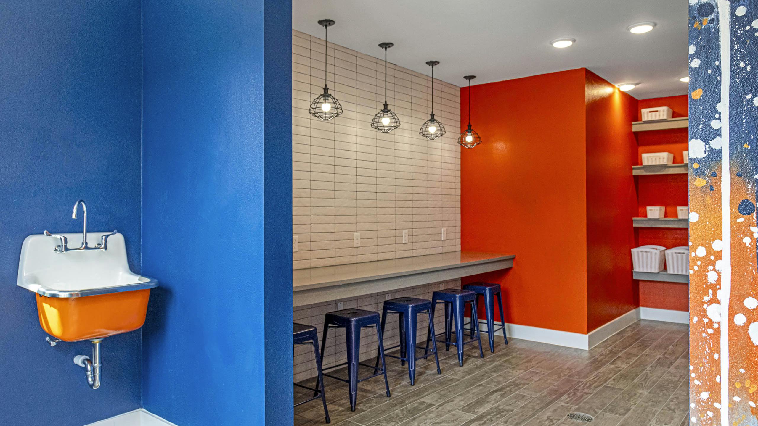 Maker space at AMLI Covered Bridge with sink and bold blue and orange walls separated by counter space with blue stools