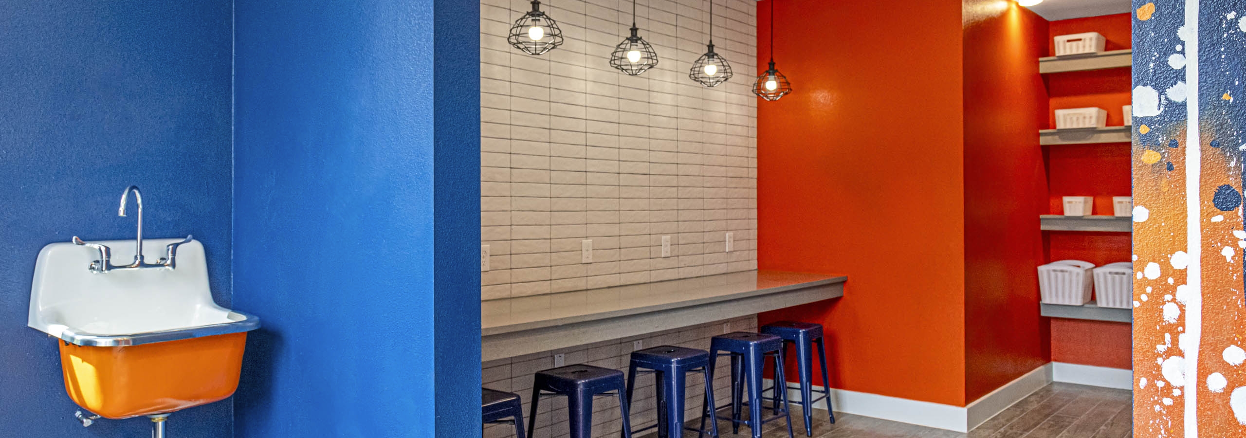 Maker space at AMLI Covered Bridge with sink and bold blue and orange walls separated by counter space with blue stools
