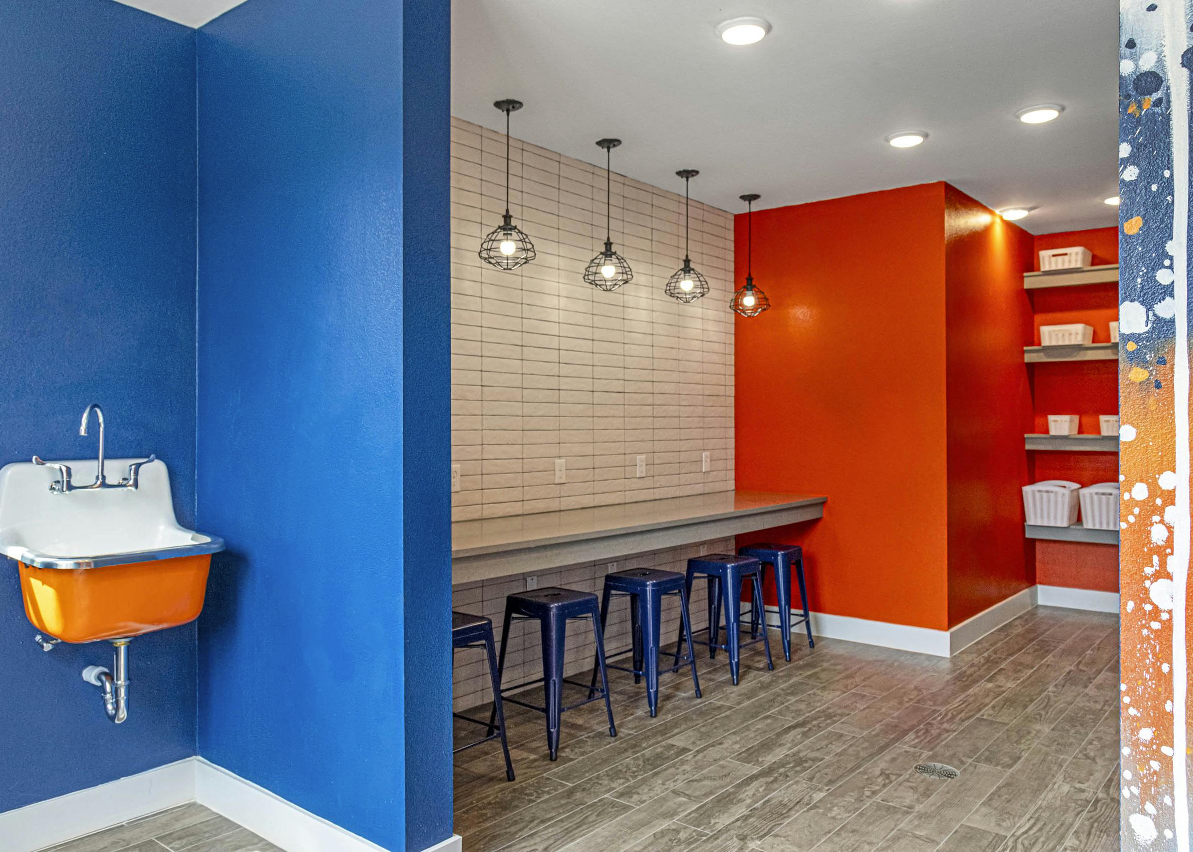 Maker space at AMLI Covered Bridge with sink and bold blue and orange walls separated by counter space with blue stools