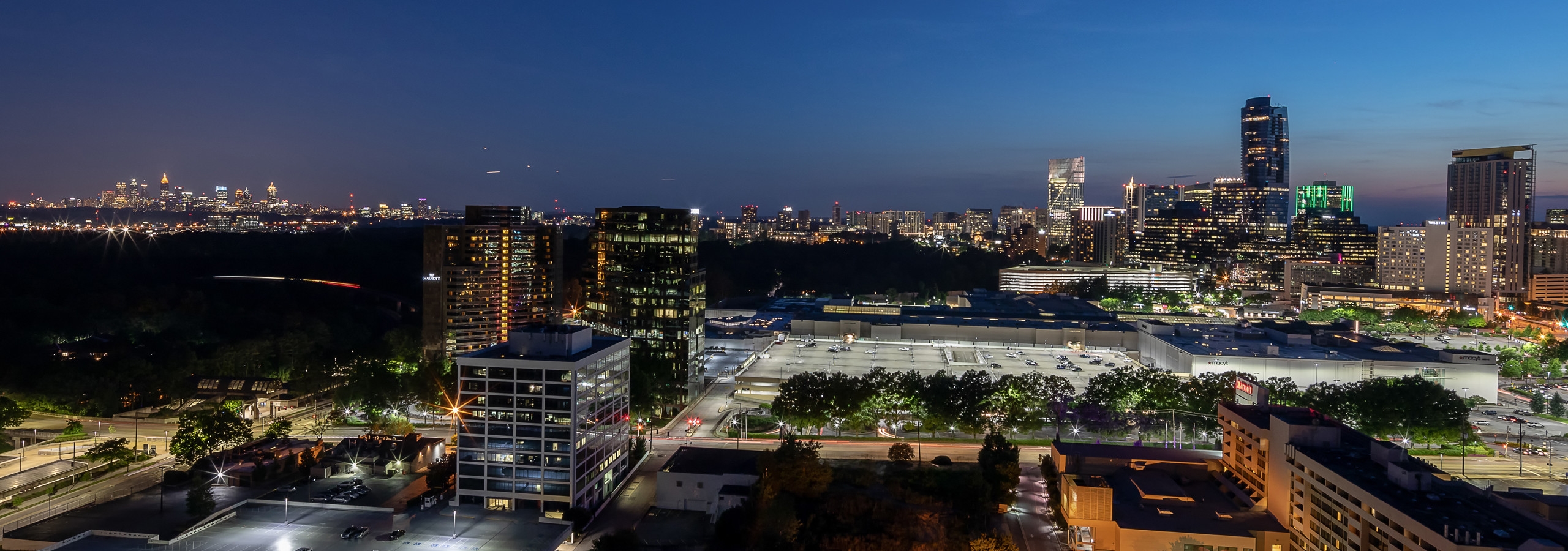 Exterior view at nighttime of the city of Atlanta with tall buildings and bright city lights throughout the image