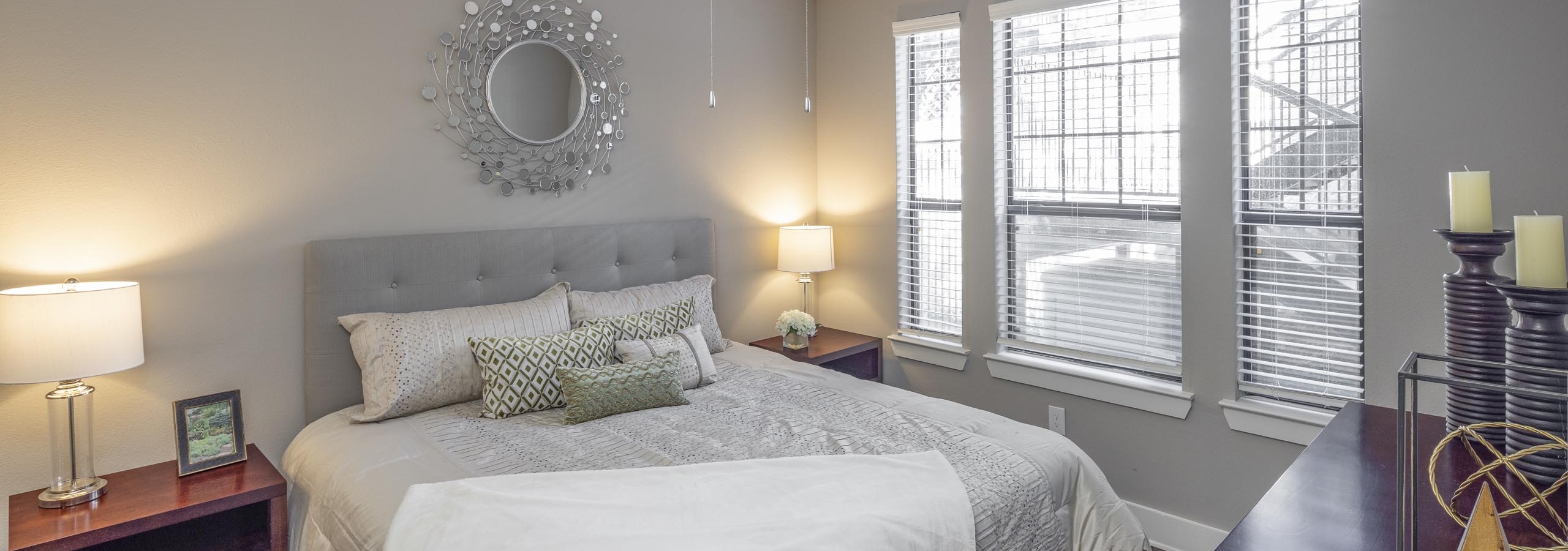 Apartment bedroom at AMLI Eastside featuring a large bed with gray bedding and wooden dressers and bedside tables