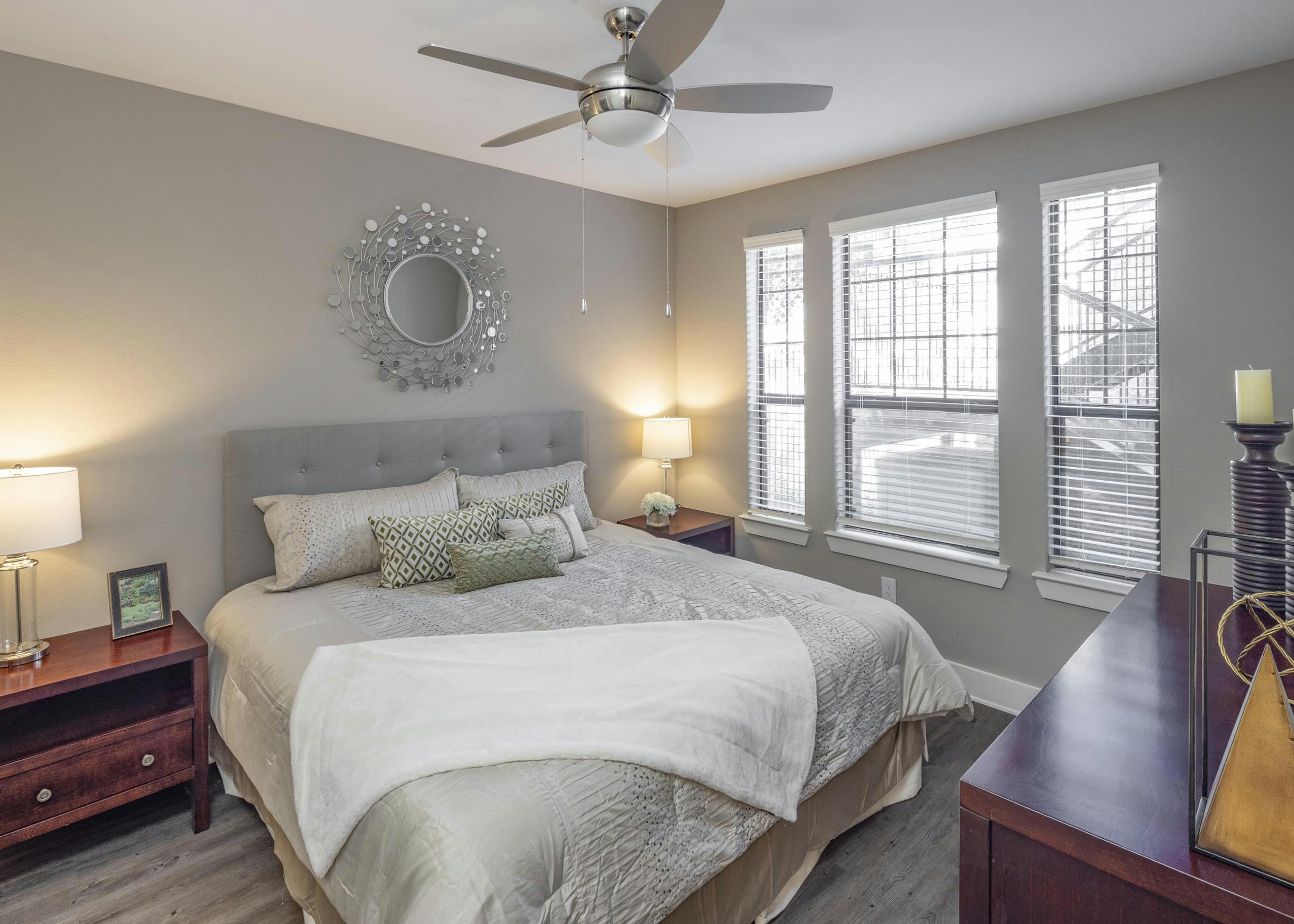 Apartment bedroom at AMLI Eastside featuring a large bed with gray bedding and wooden dressers and bedside tables