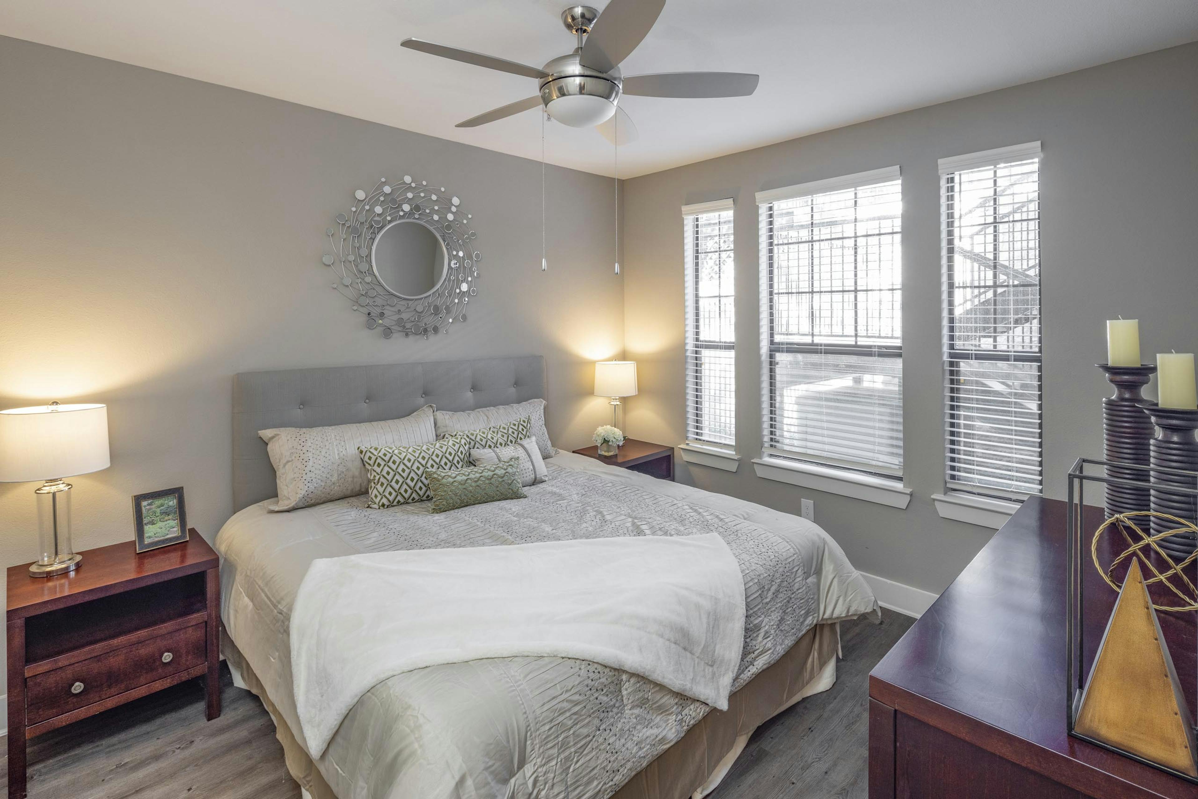 Apartment bedroom at AMLI Eastside featuring a large bed with gray bedding and wooden dressers and bedside tables