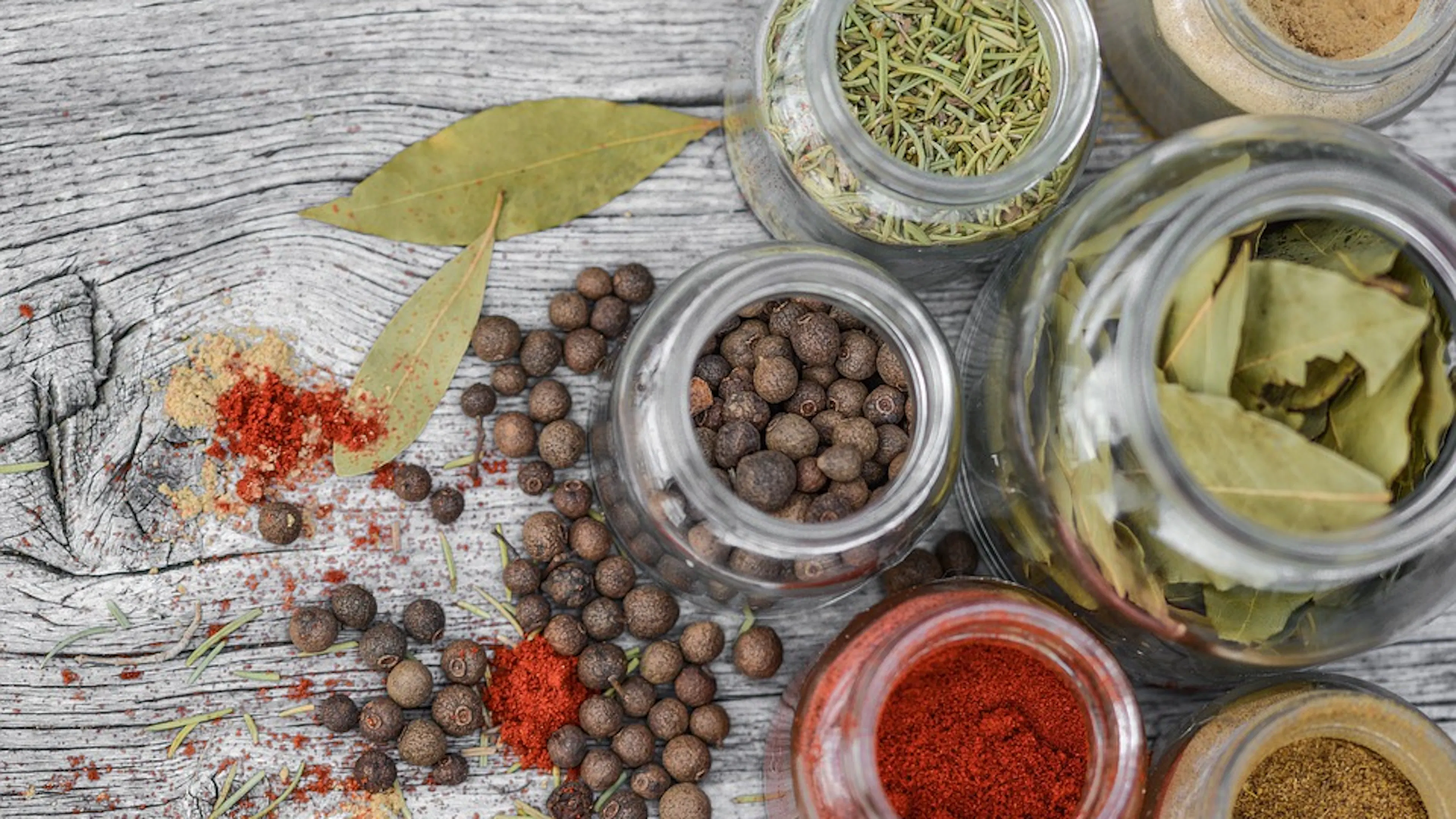 A few glass jars photographed from above filled with whole spices all set on a wooden table