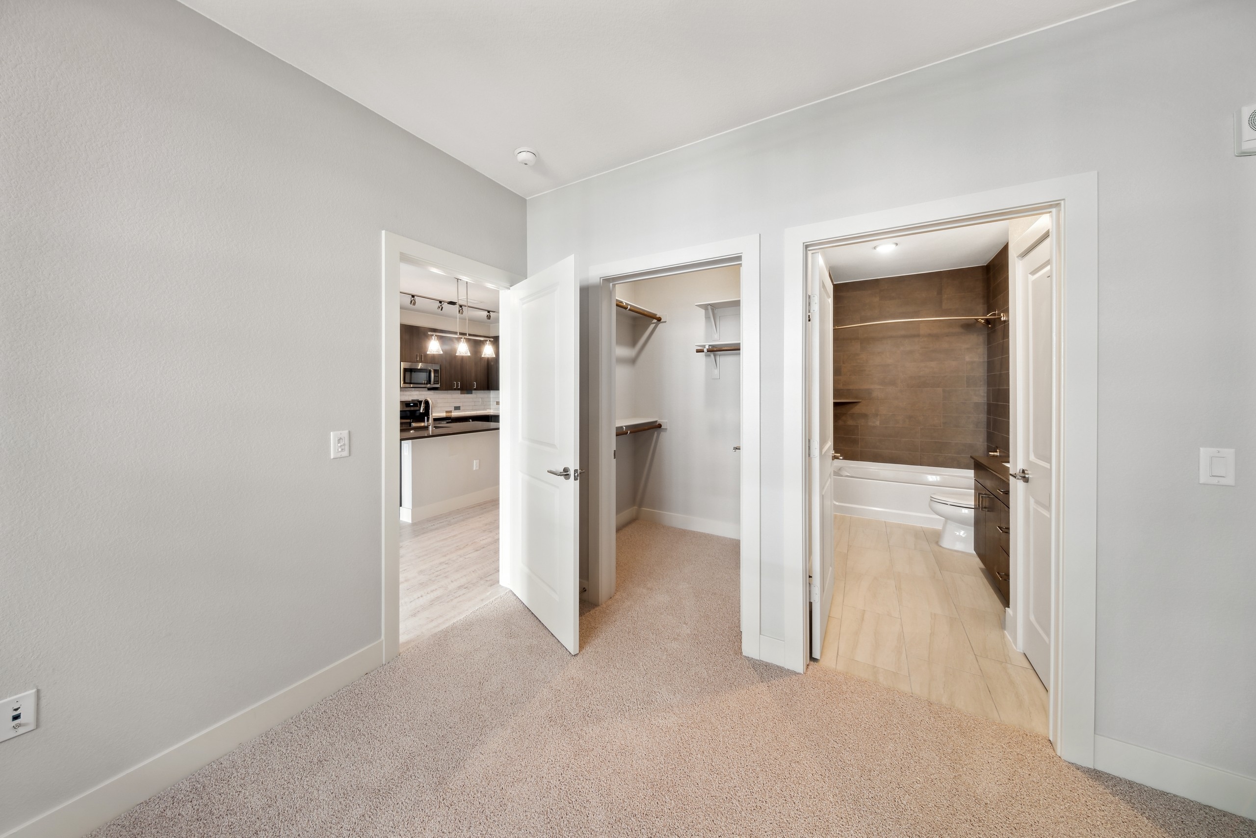 AMLI RiNo apartment bedroom with bathroom with brown tile surround and walk in closet and view to kitchen with pendant lights