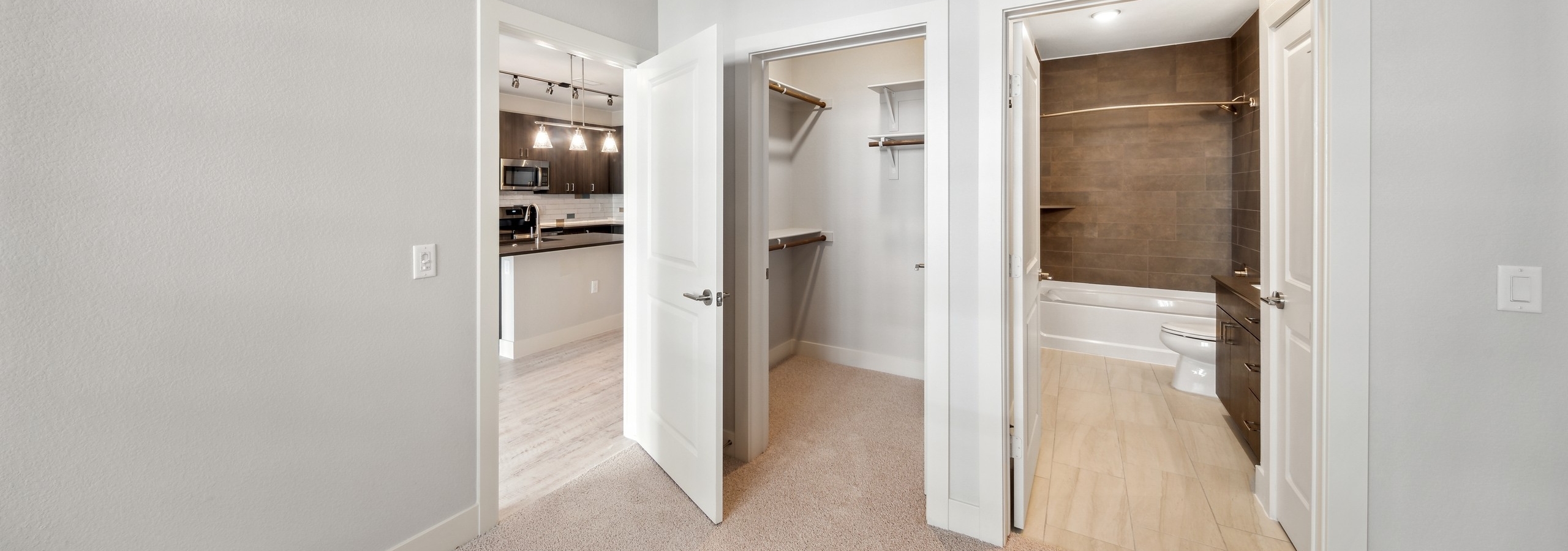 AMLI RiNo apartment bedroom with bathroom with brown tile surround and walk in closet and view to kitchen with pendant lights