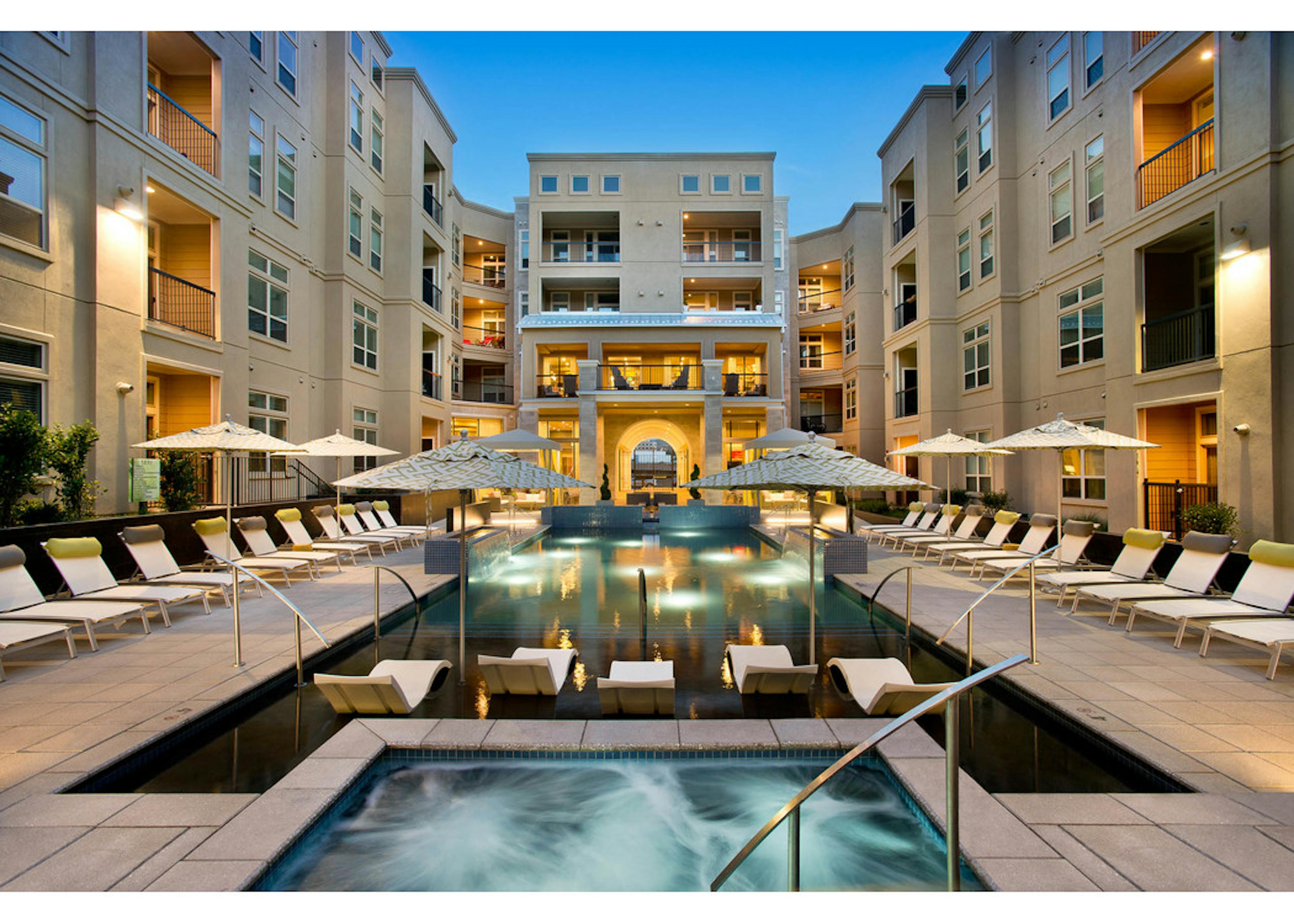 Exterior dusk view of pool close-up with water ledge loungers, steamy Jacuzzi and umbrellas at AMLI RidgeGate apartments