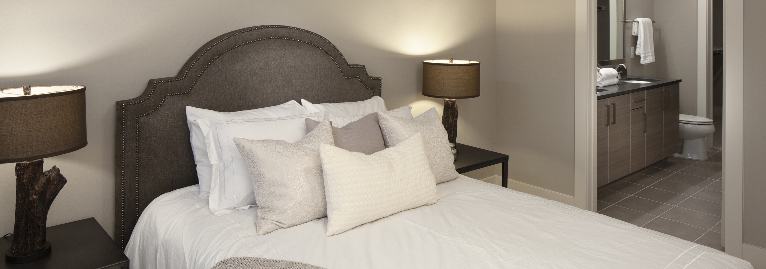 Interior view of a bedroom at AMLI Riverfront green apartments with stylish lamps as well as a peek into the bathroom