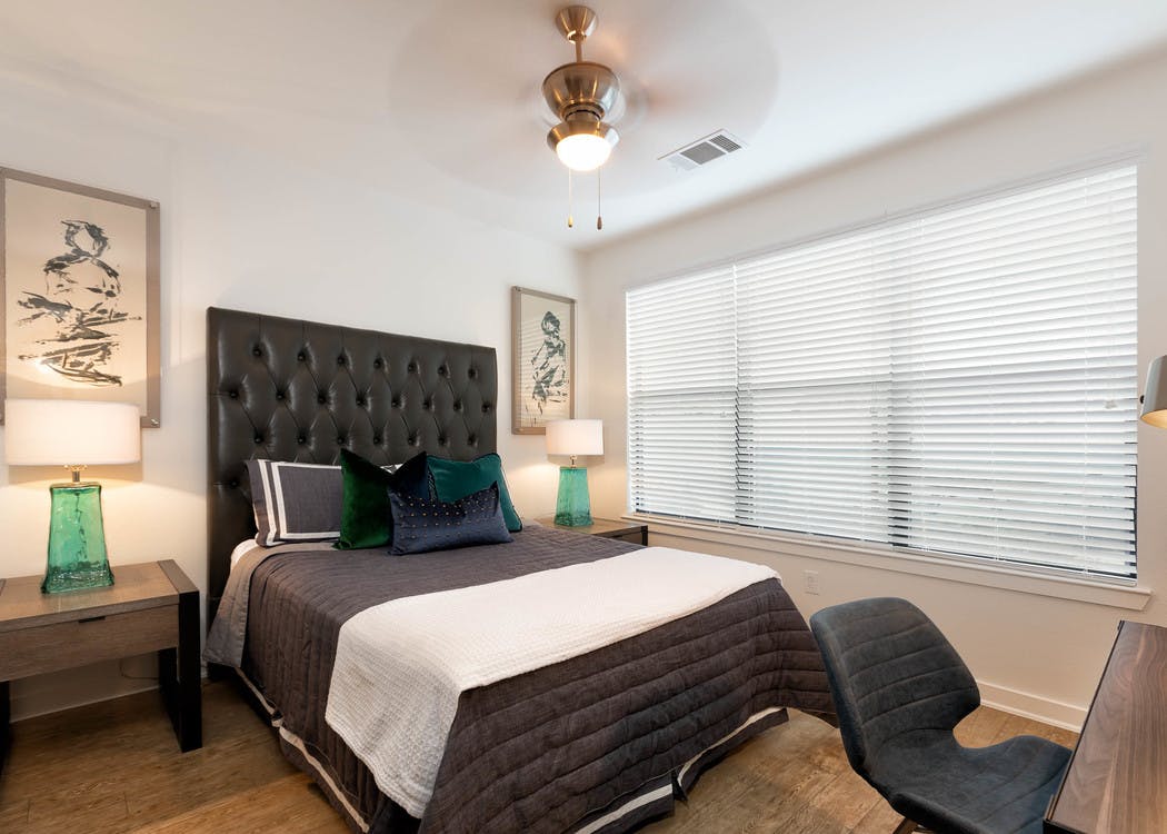 Bedroom at AMLI Quadrangle with a tall leather headboard with black bedding and white walls with a large window with blinds