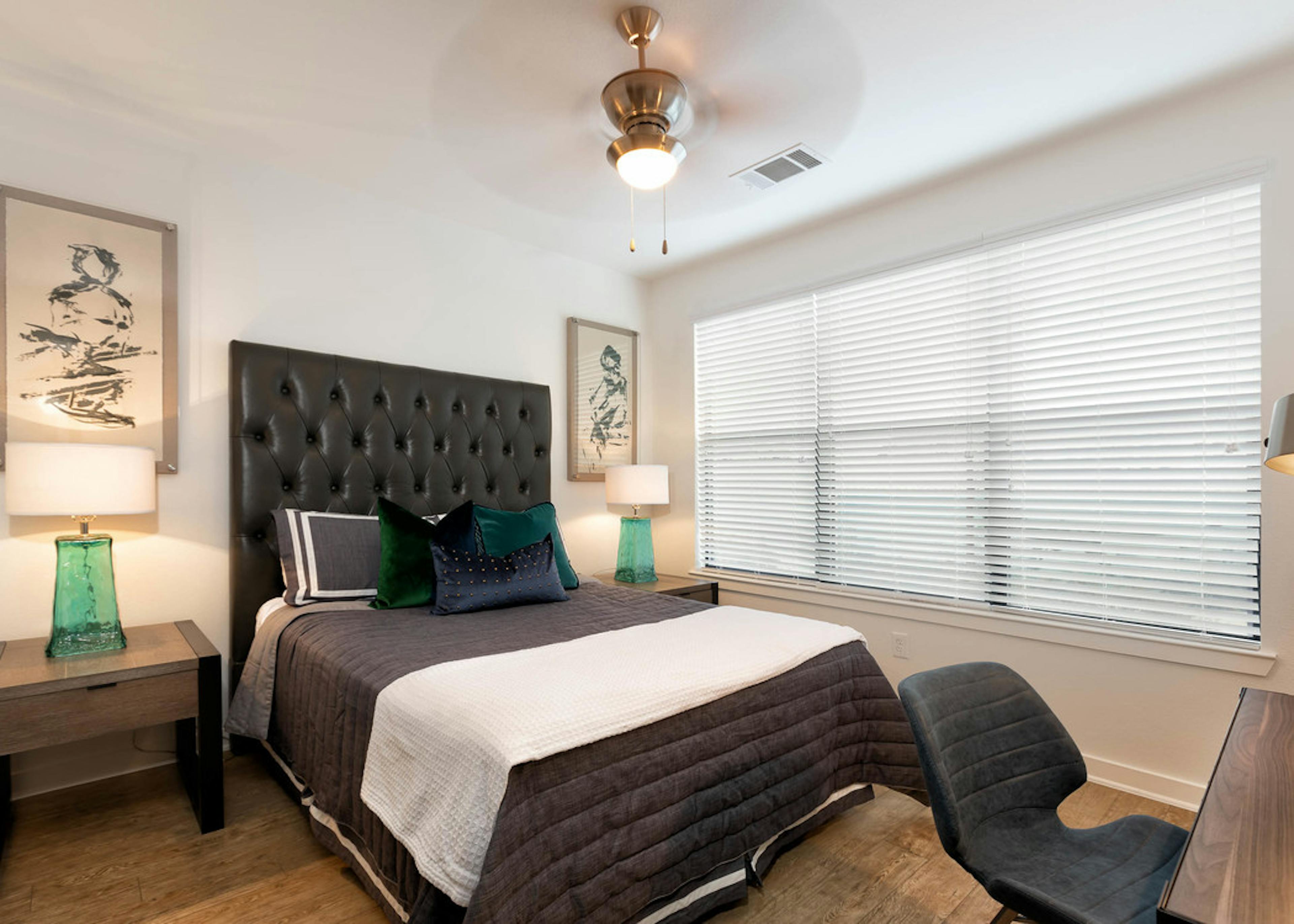 Bedroom at AMLI Quadrangle with a tall leather headboard with black bedding and white walls with a large window with blinds