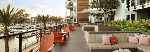 Daytime view of AMLI Marina Del Rey apartment elevated outdoor lounge with cozy seating overlooking the marina and palm trees