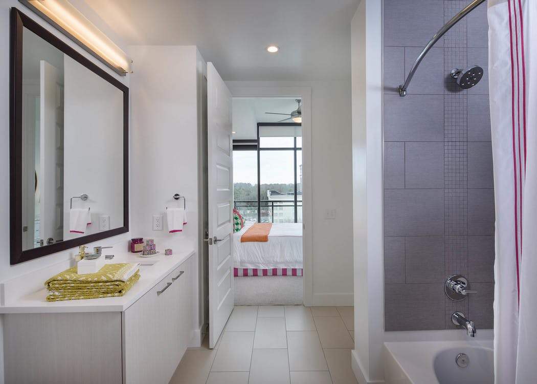 Bathroom at AMLI 3464 with white vanity sink and a grey tiled shower with an open door peaking into the connected bedroom