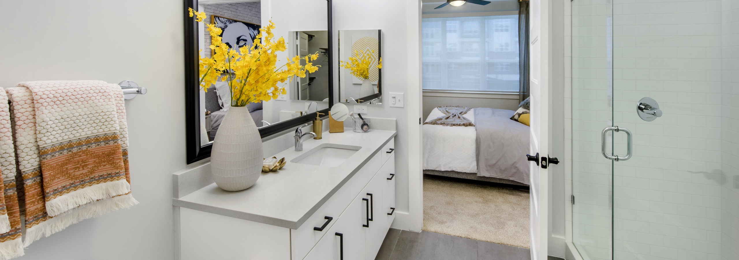 AMLI Decatur apartment bathroom with quartz countertop on a white wood vanity with a framed mirror and frameless glass shower