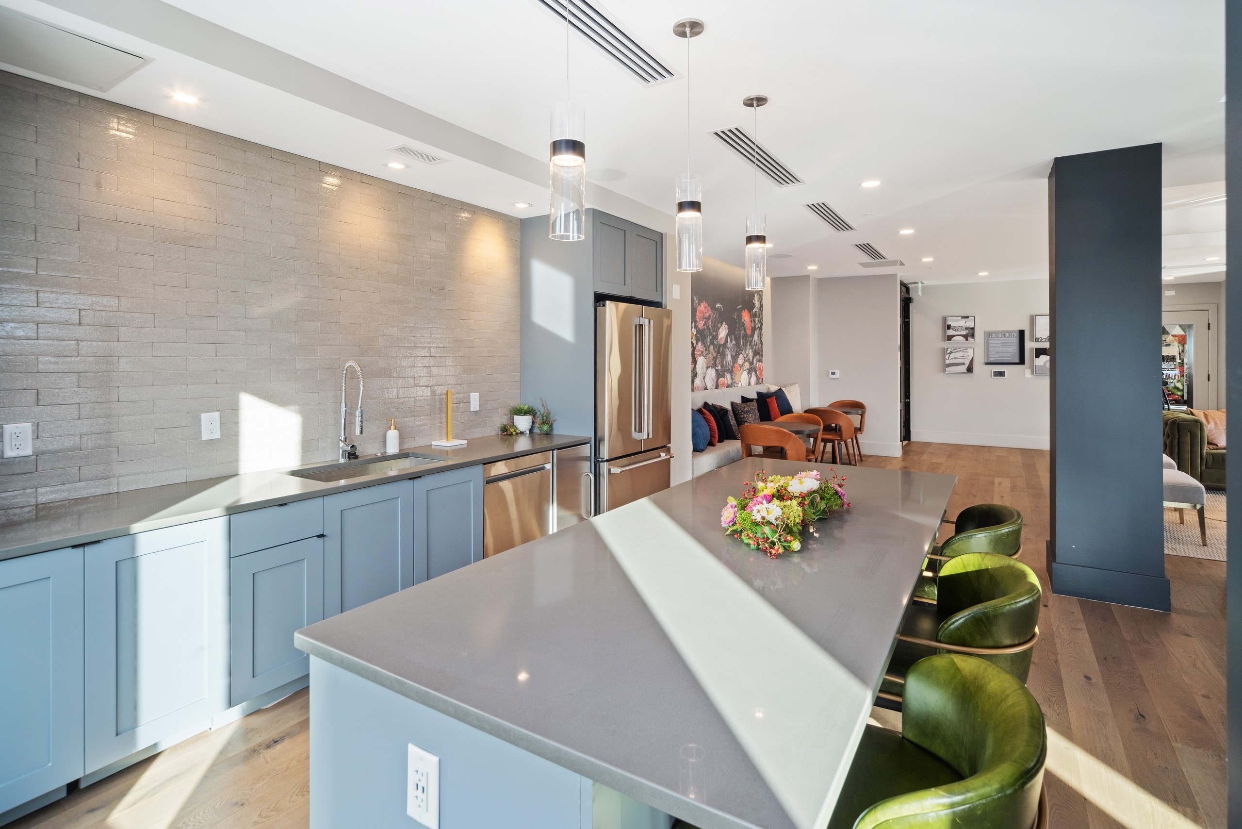 Modern AMLI at Uptown resident lounge kitchen with blue cabinetry and grey countertops featuring pendant lights above island