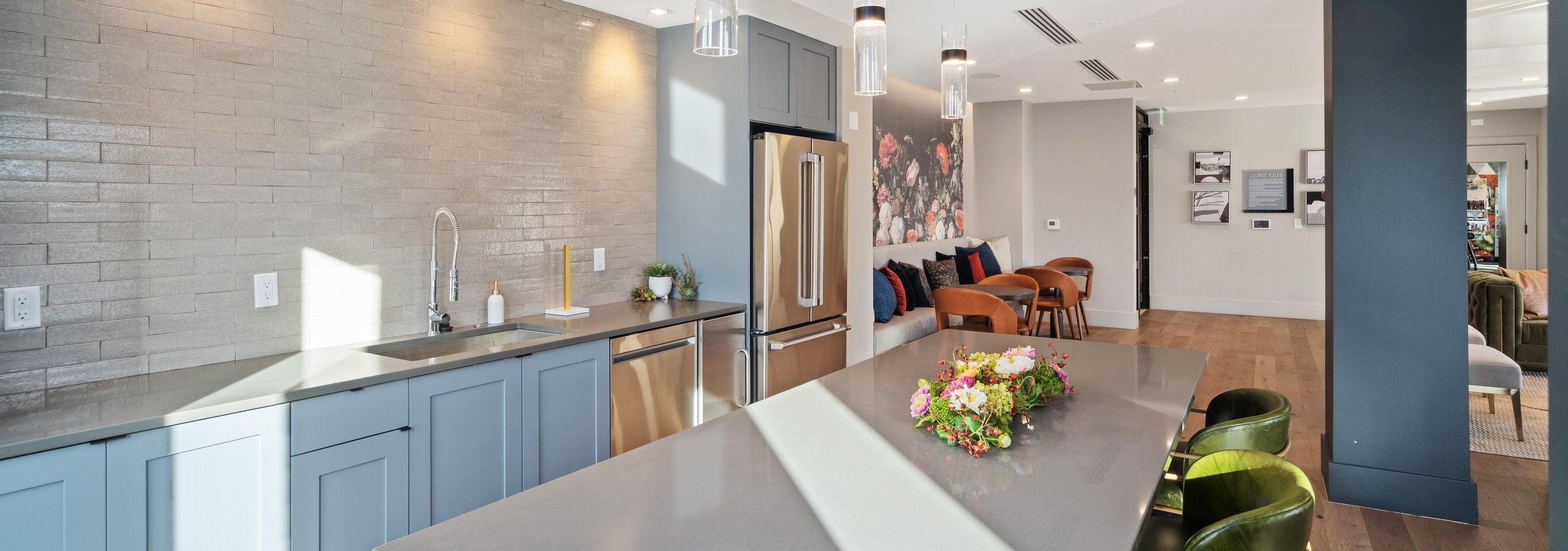 Modern AMLI at Uptown resident lounge kitchen with blue cabinetry and grey countertops featuring pendant lights above island