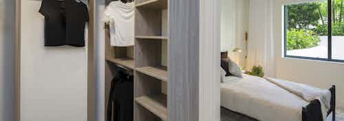 Interior view of AMLI Midtown Miami apartment walk in closet with wood shelving, and marble floors and view into the bedroom