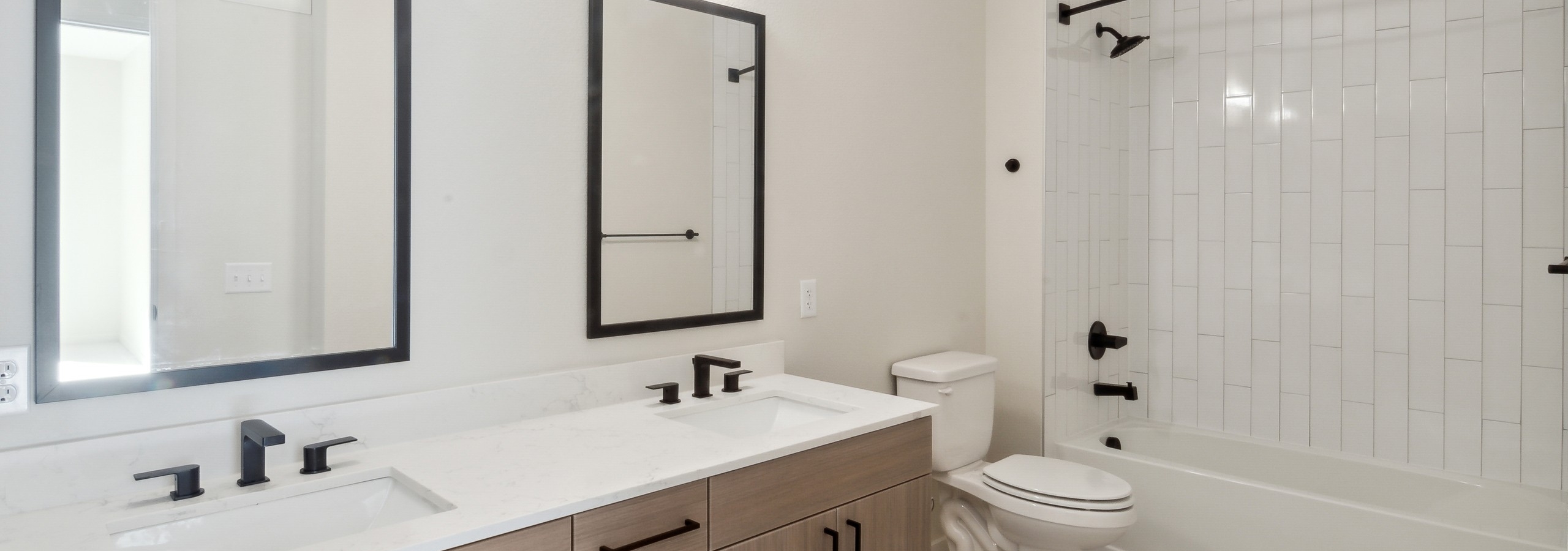 Bathroom at AMLI Broadway Park with double wood grain vanity with white countertops and 2 black mirrors and white soaking tub