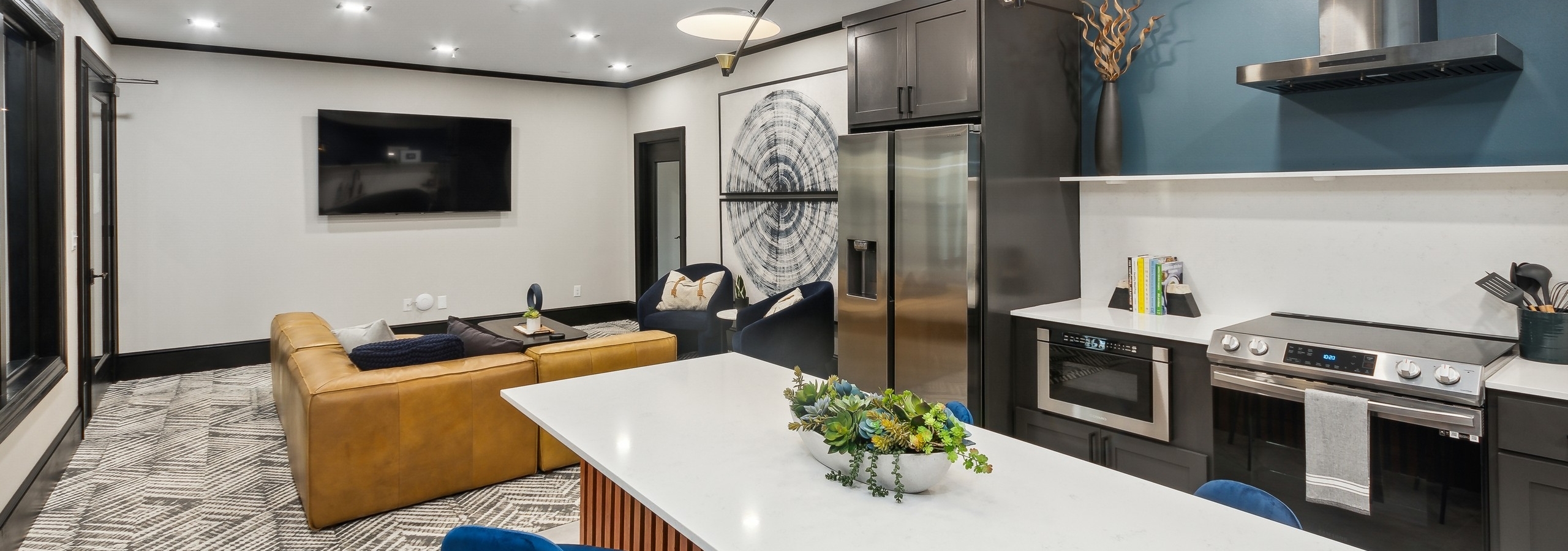 Resident lounge at AMLI Campion Trail with caramel couch facing large screen TV on white wall and island kitchen in foreground