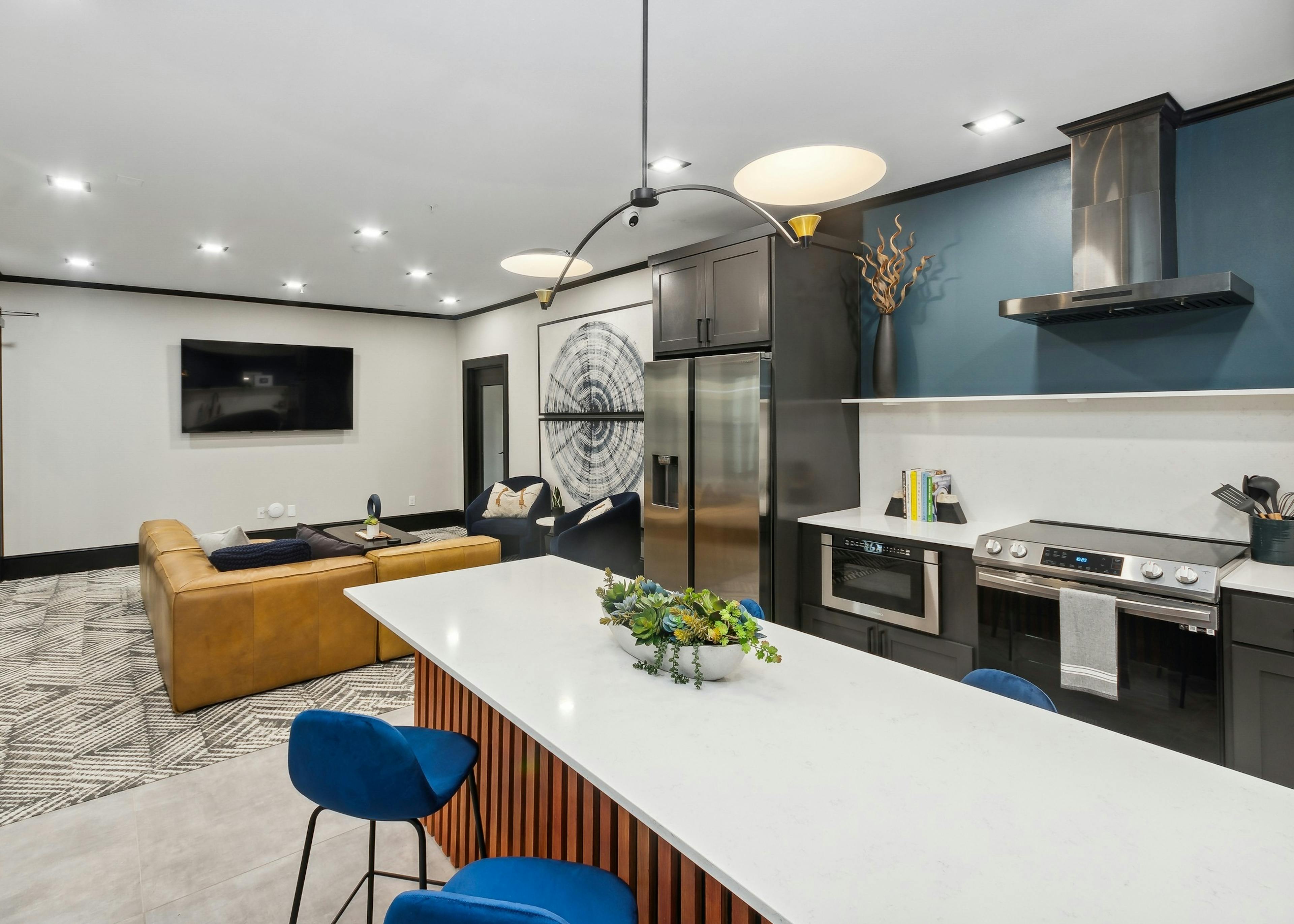 Resident lounge at AMLI Campion Trail with caramel couch facing large screen TV on white wall and island kitchen in foreground