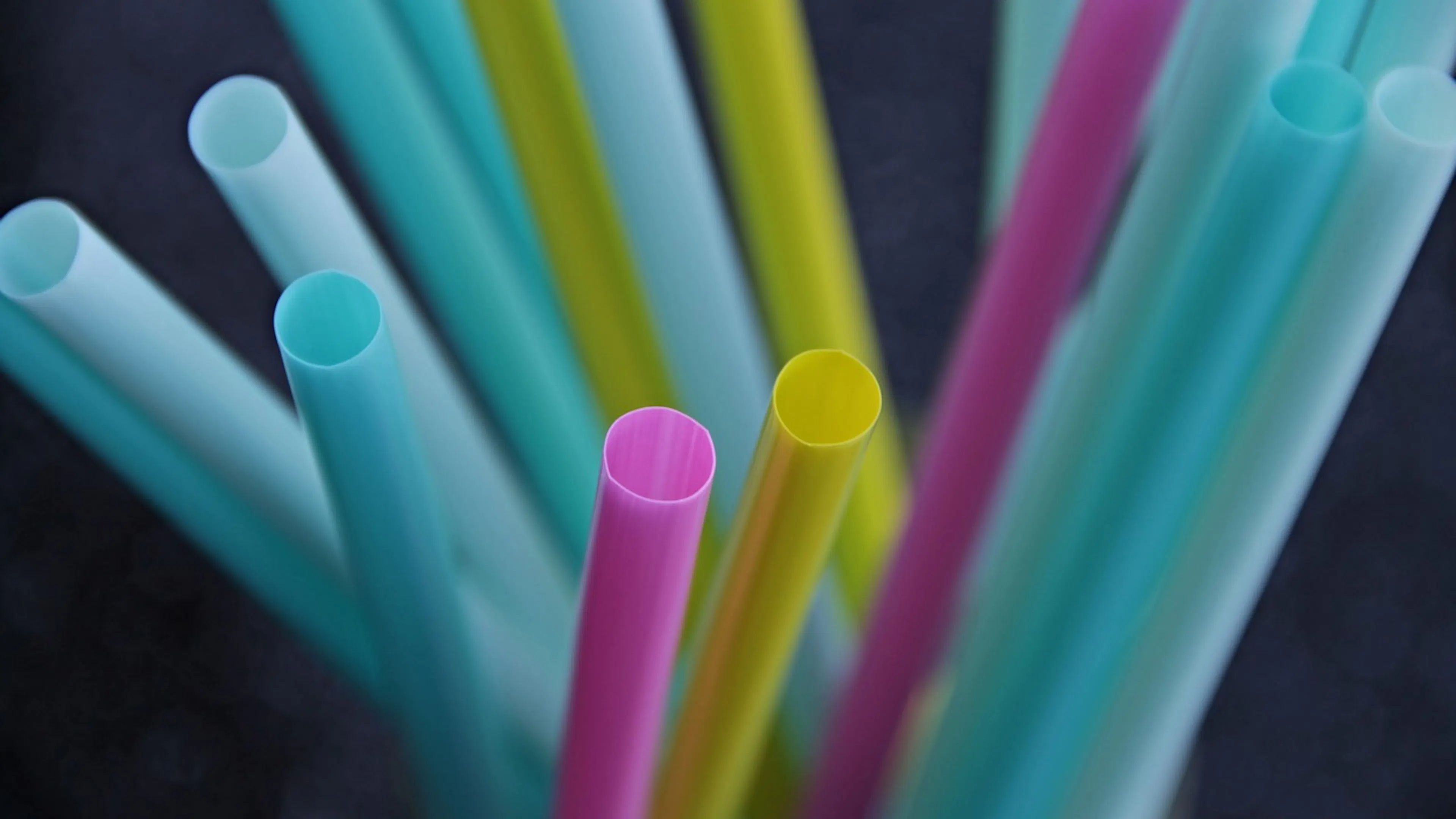 A close up of a small handful of plastic straws focusing on a pink straw