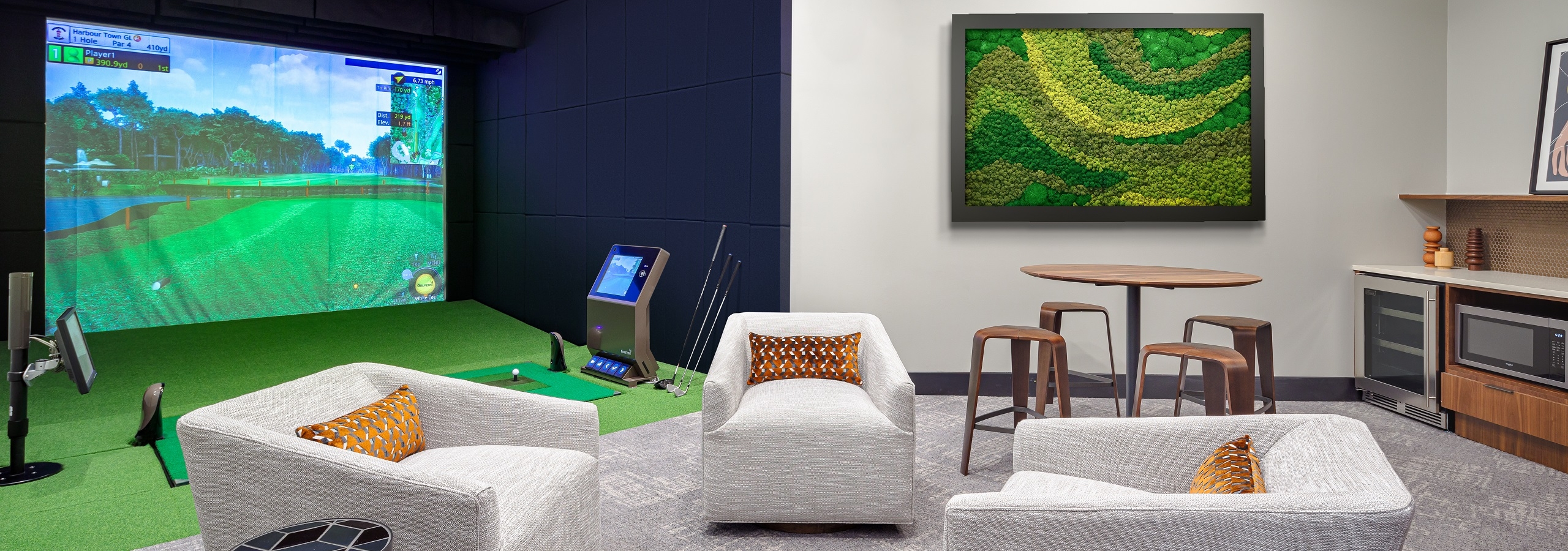 AMLI Fountain Place golf simulator with large screen with golf scene and lounge with 3 comfy chairs and table with 4 stools