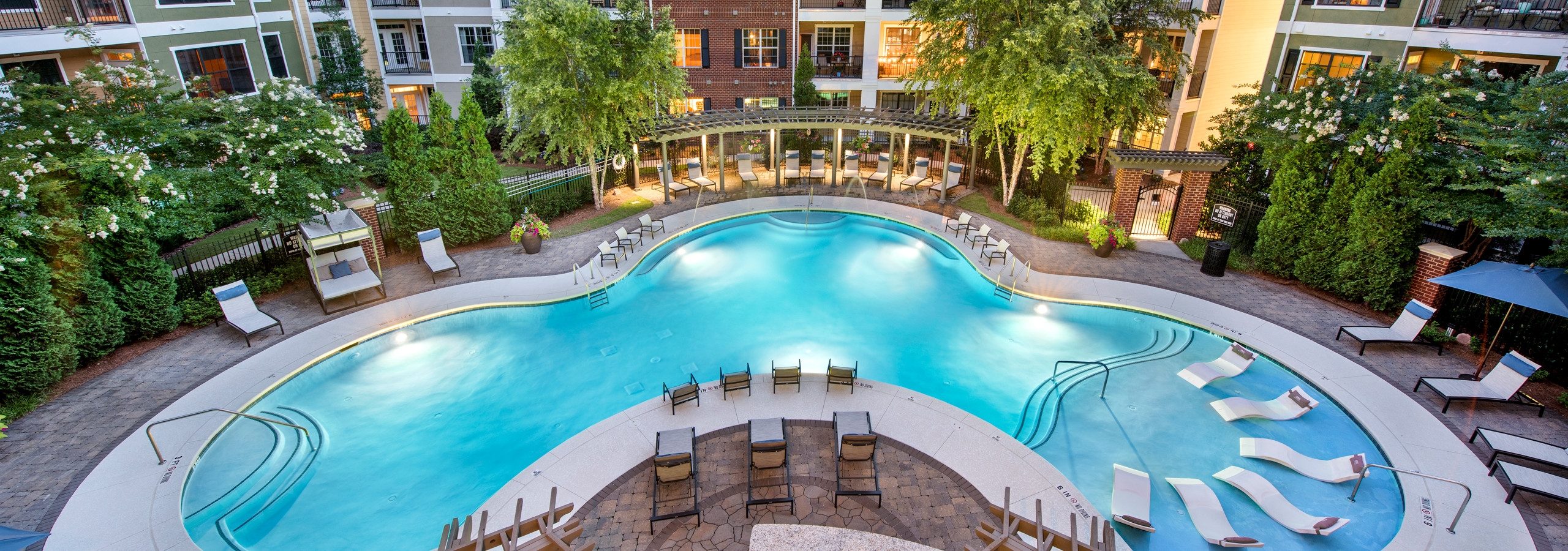 Lagoon swimming pool at AMLI North Point with clean blue water surrounded by thriving trees and white lounge chairs