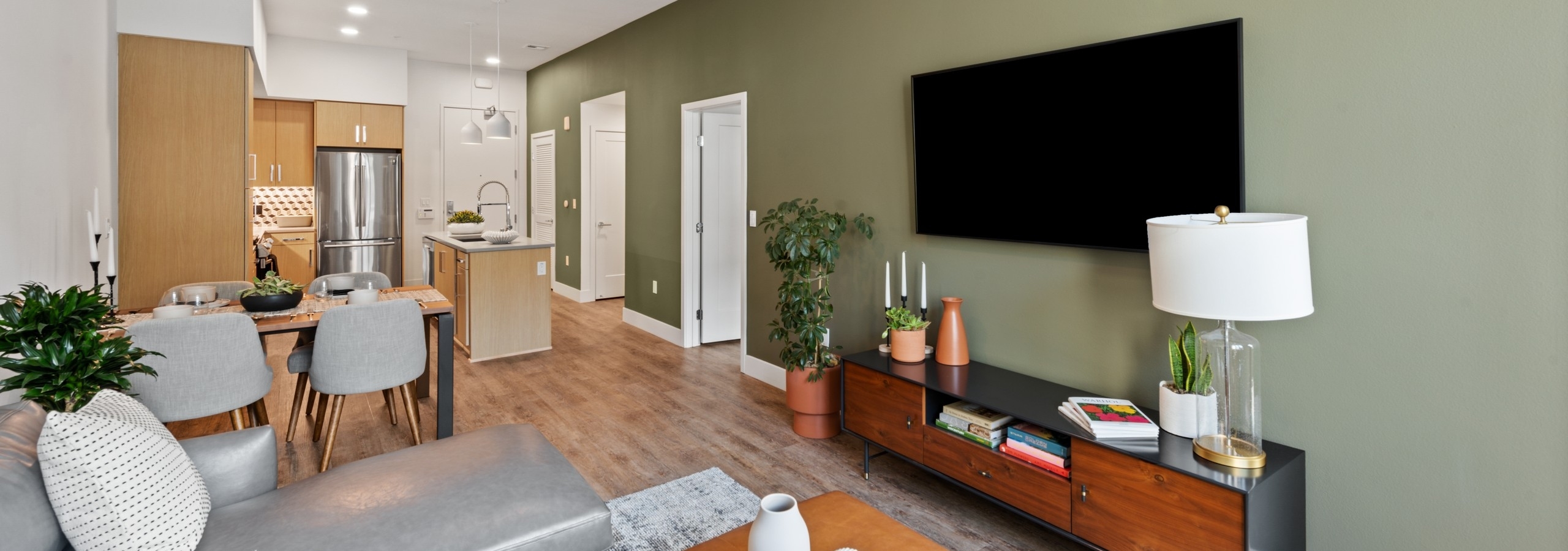 Interior view of AMLI Old Pasadena apartment living room with gray sofa and hardwood floors and big screen TV and dining table