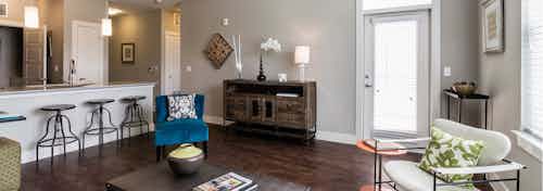 Interior view of a living room at AMLI Arista apartments with chairs and tables as well as a view of the kitchen with stools