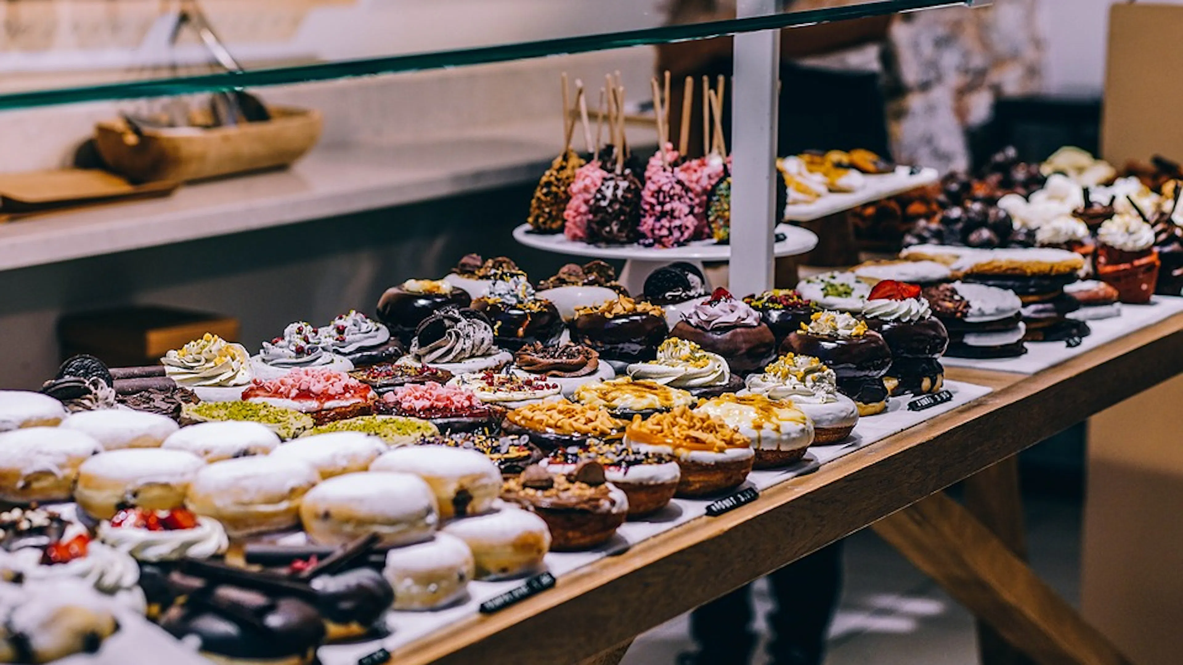 A long wooden table covered with artisan doughnuts like chocolate and strawberry and candy covered and custard filled